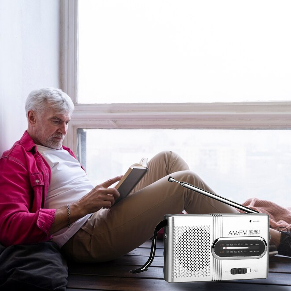 Mann liest ein Buch neben einem silbernen Radio mit Antenne. Fenster im Hintergrund.
