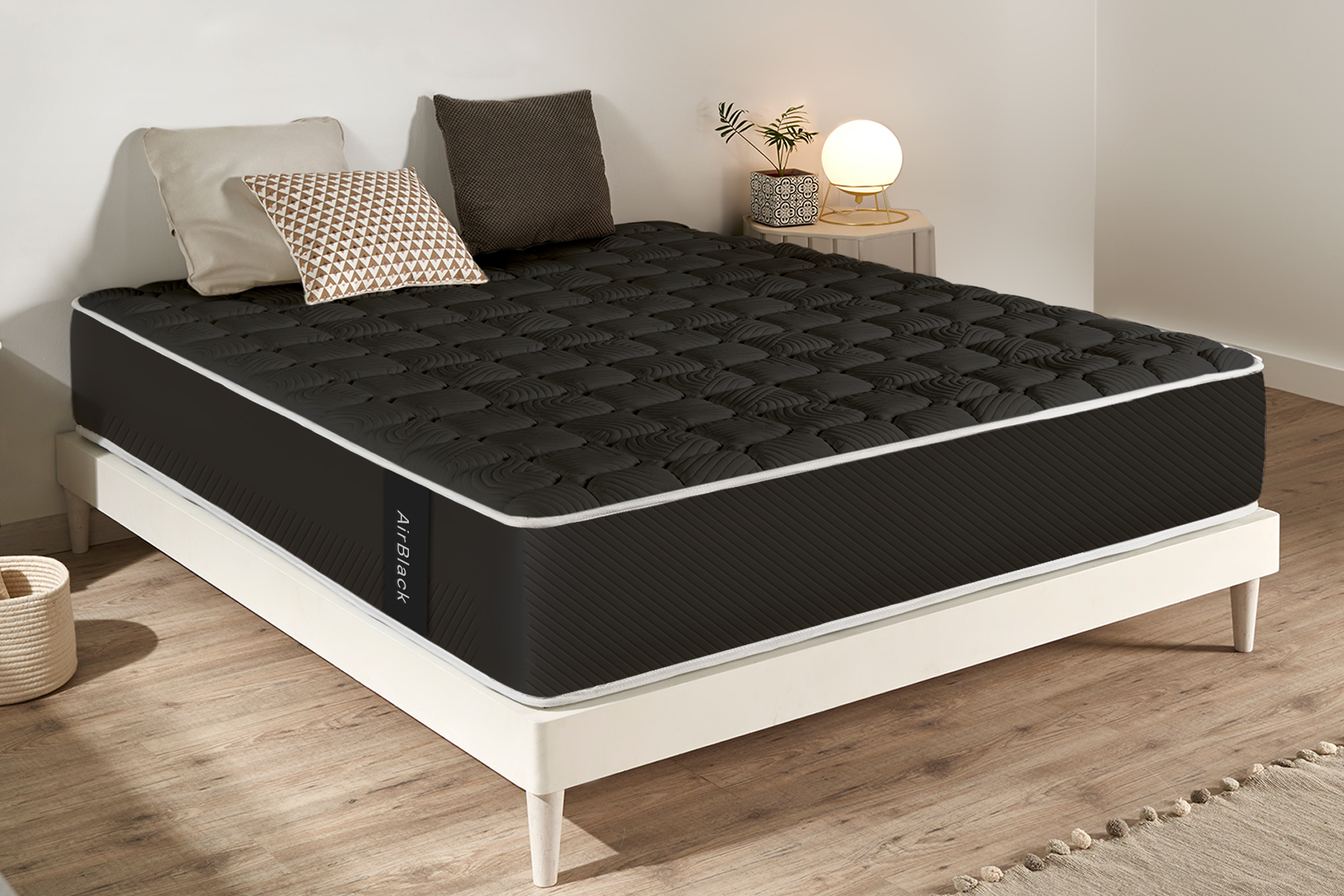 Colchón negro con ribete blanco en un marco de cama blanco. Almohadas y una lámpara están cerca.
