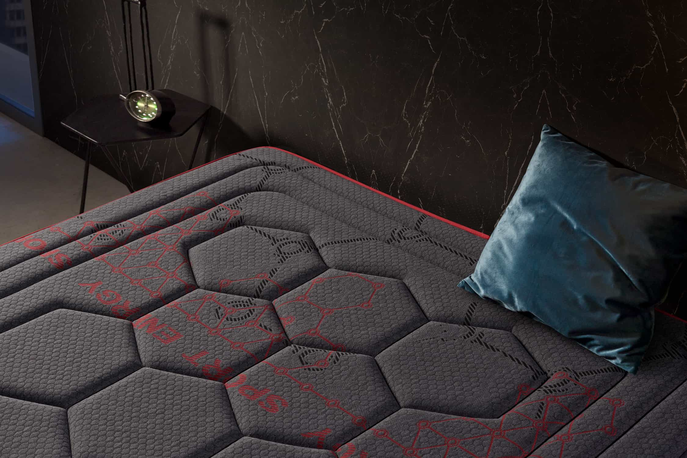 Primer plano de un colchón gris oscuro con diseño de hexágonos rojos. Se ve una almohada azul.