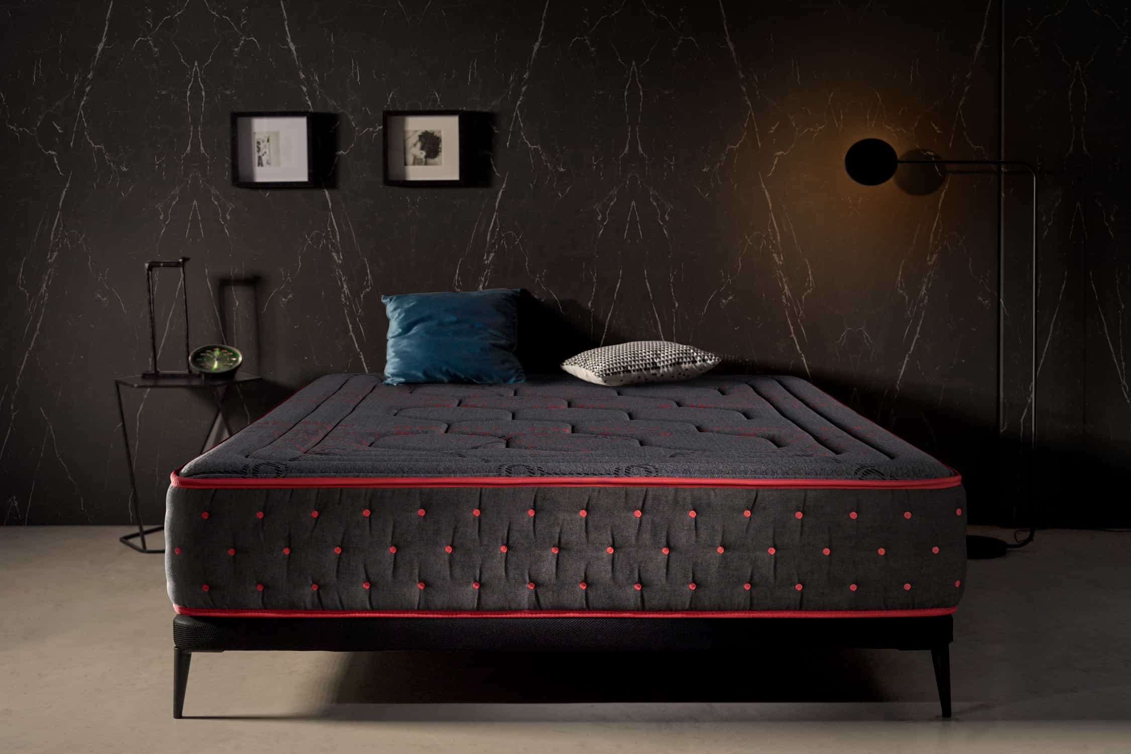 Un dormitorio oscuro con una cama negra y un colchón gris oscuro con ribete rojo.