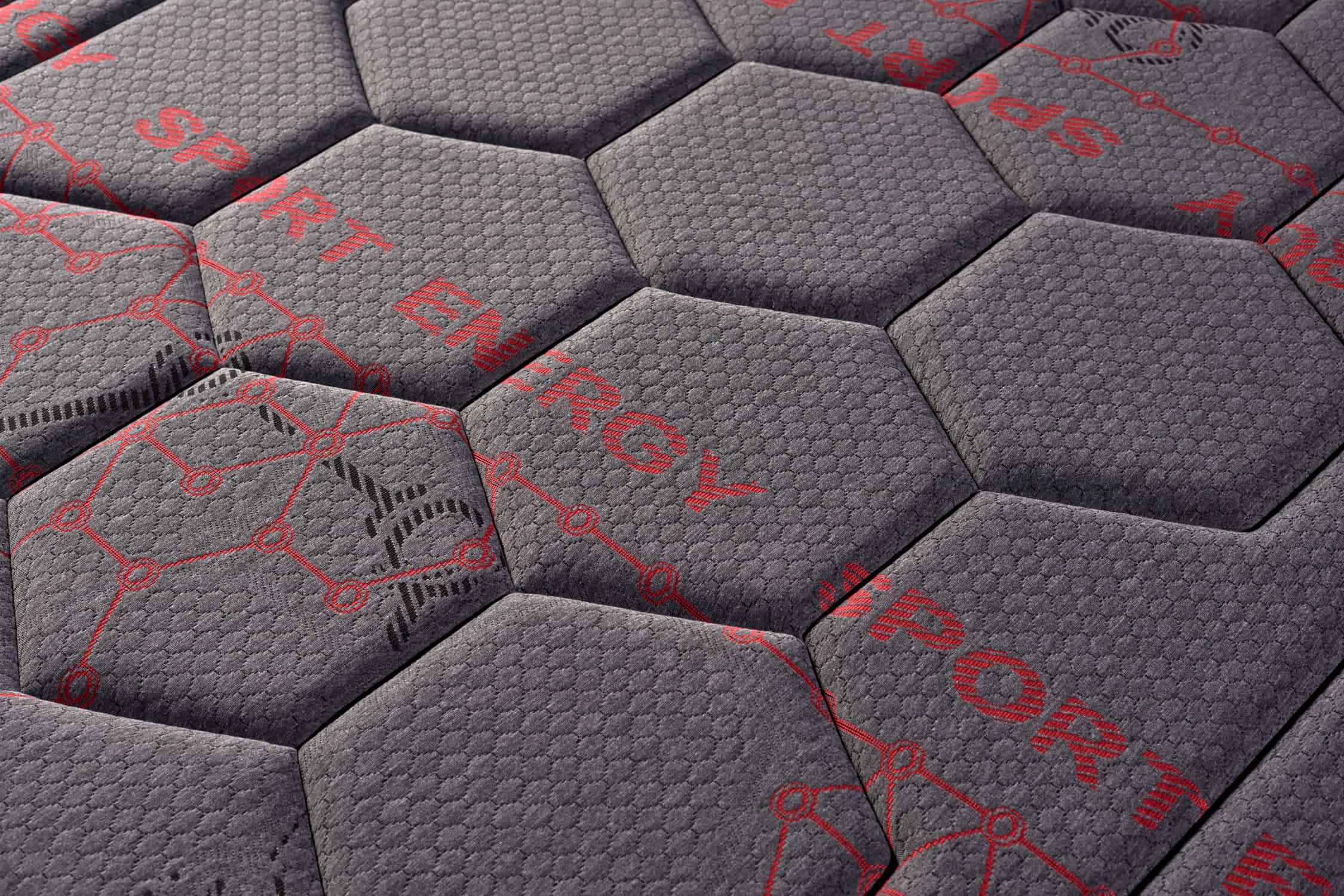 Primer plano de un colchón gris con patrón hexagonal y detalles rojos, etiquetado como 'SPORT ENERGY'.