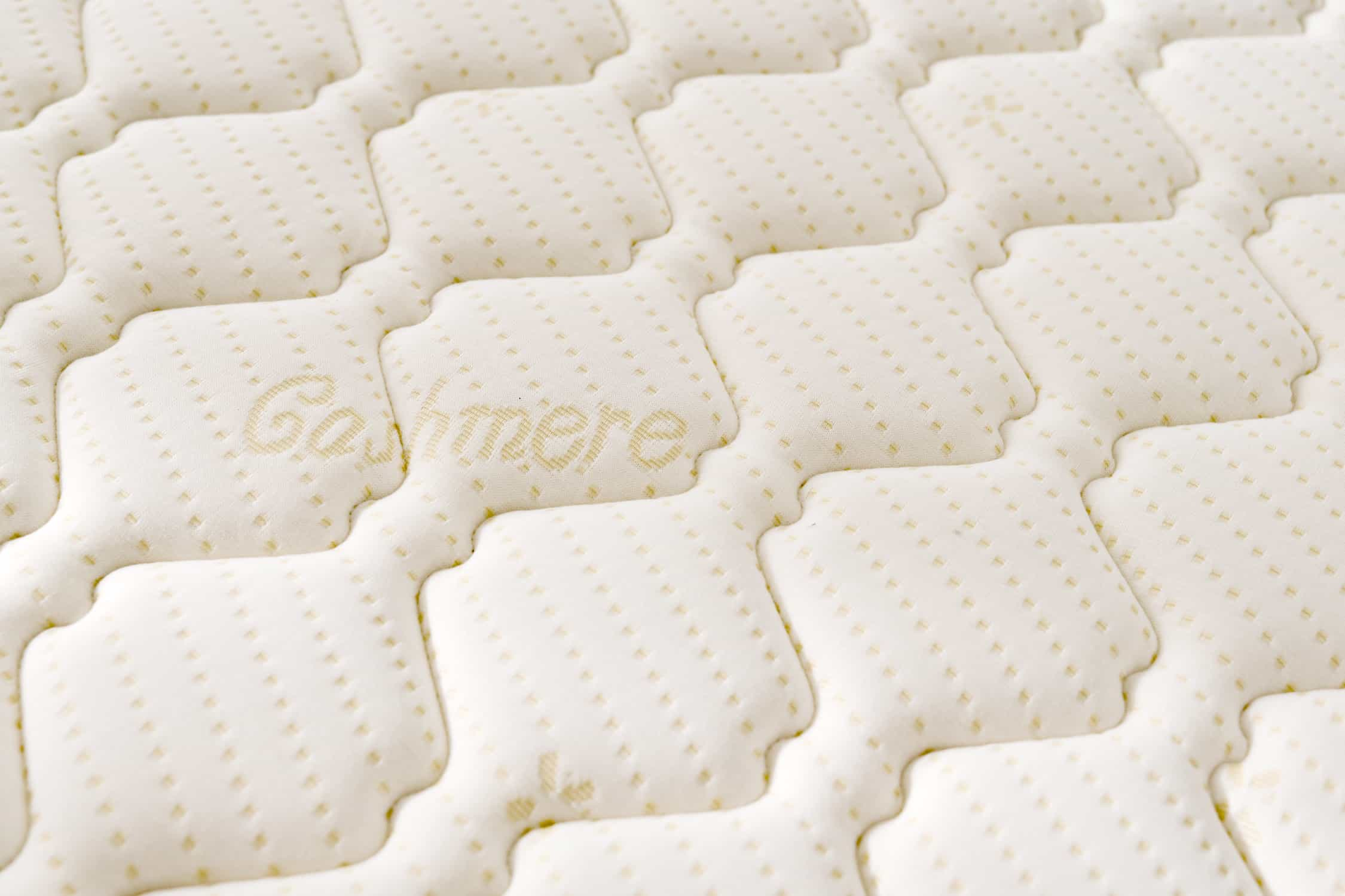 Primer plano de una superficie de colchón blanco con un patrón acolchado repetido. La palabra 'Cashmere' está bordada.