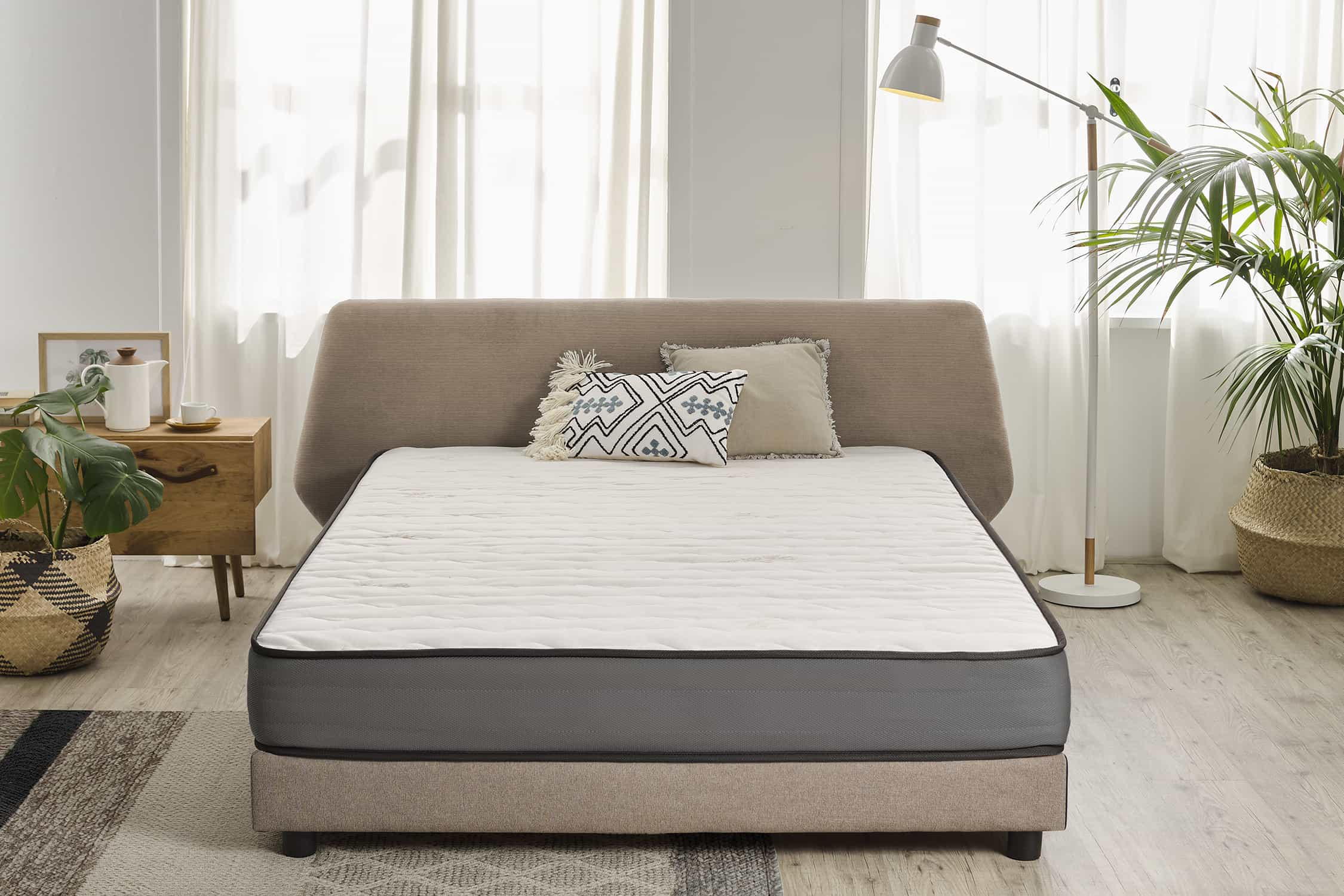 Colchón en un ambiente de habitación con marco de cama, almohadas y mesita de noche.