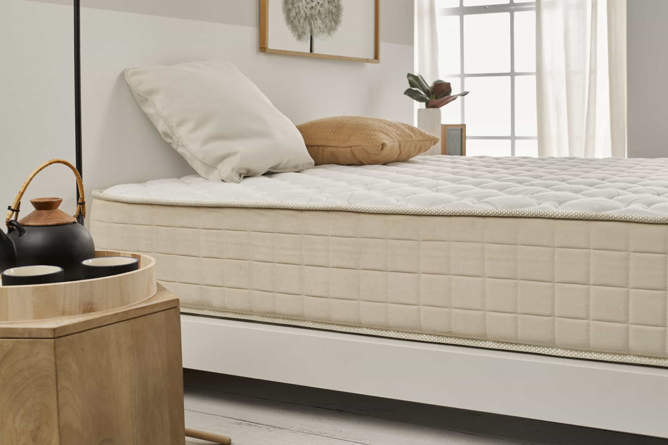 Escena de dormitorio con colchón beige sobre cama blanca. Dos almohadas en la cama.