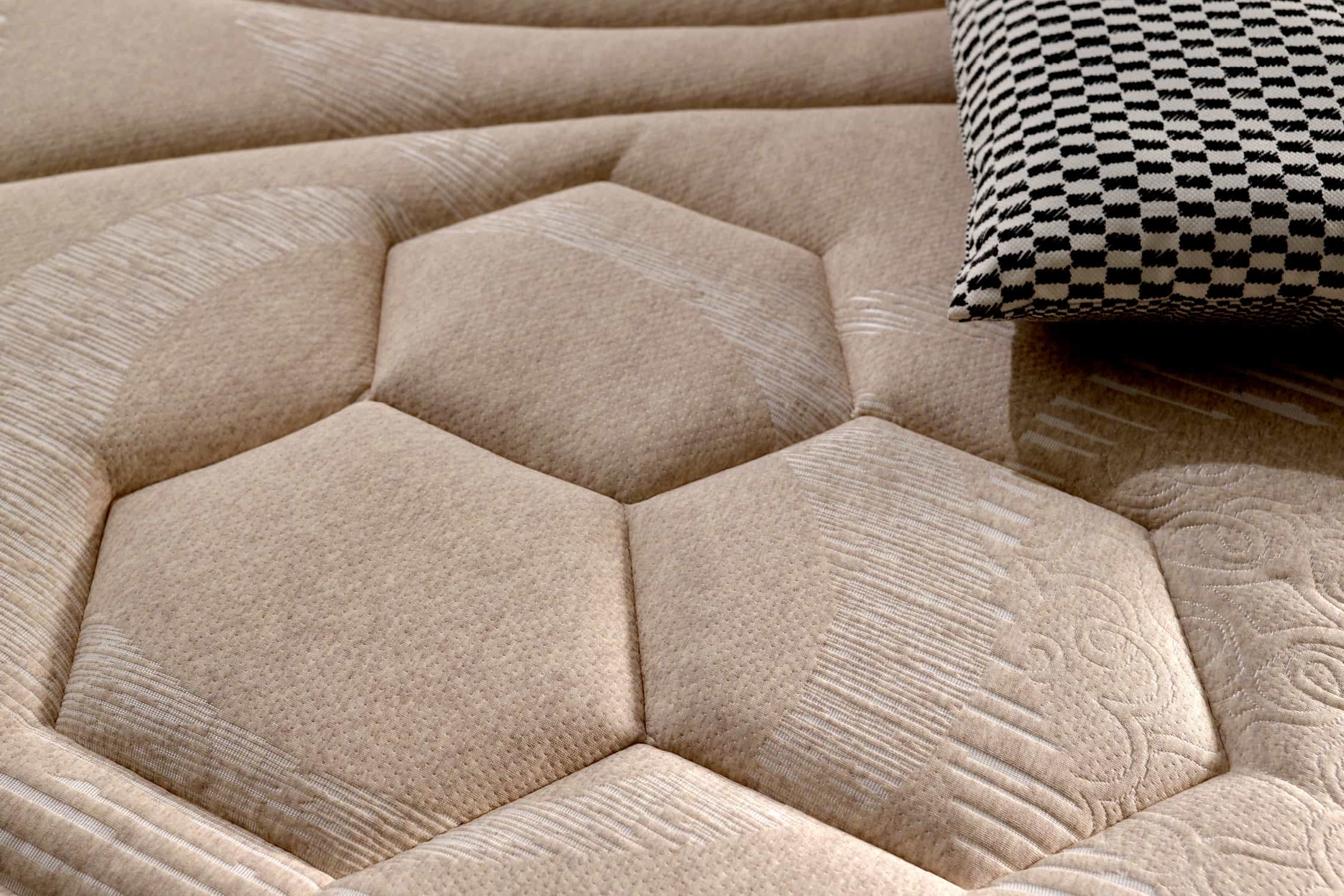 Primer plano de un colchón beige con patrón de panal y una almohada.