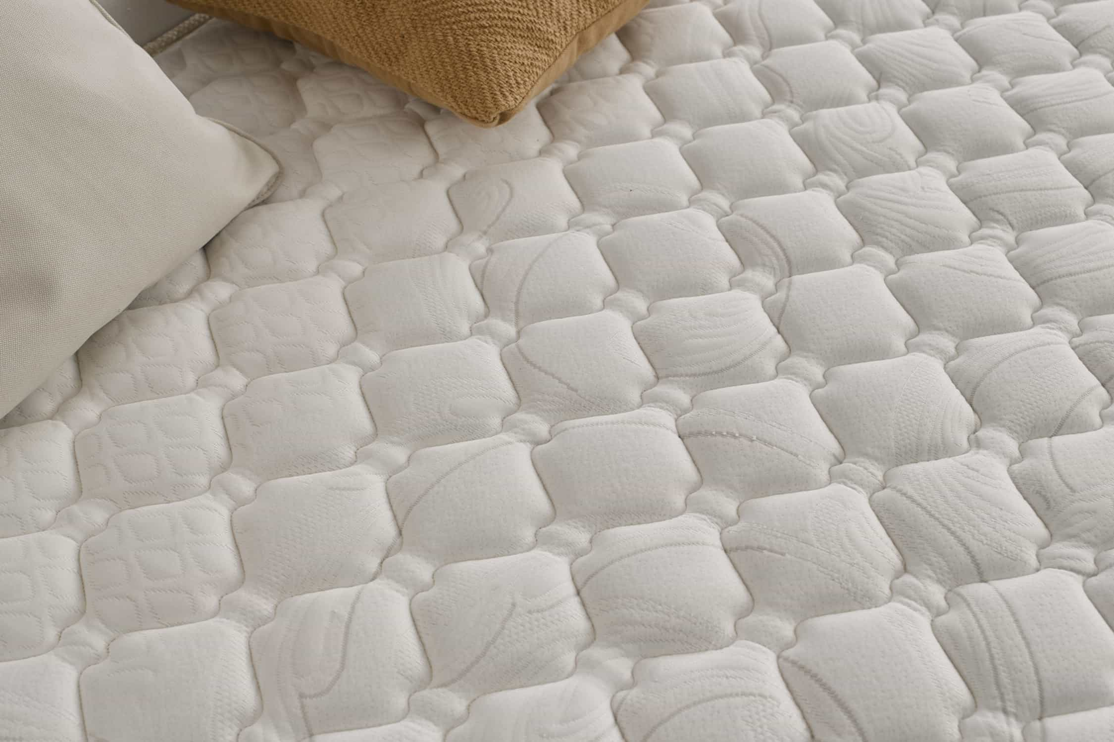 Primer plano de un colchón blanco con patrón cuadrado y almohadas.