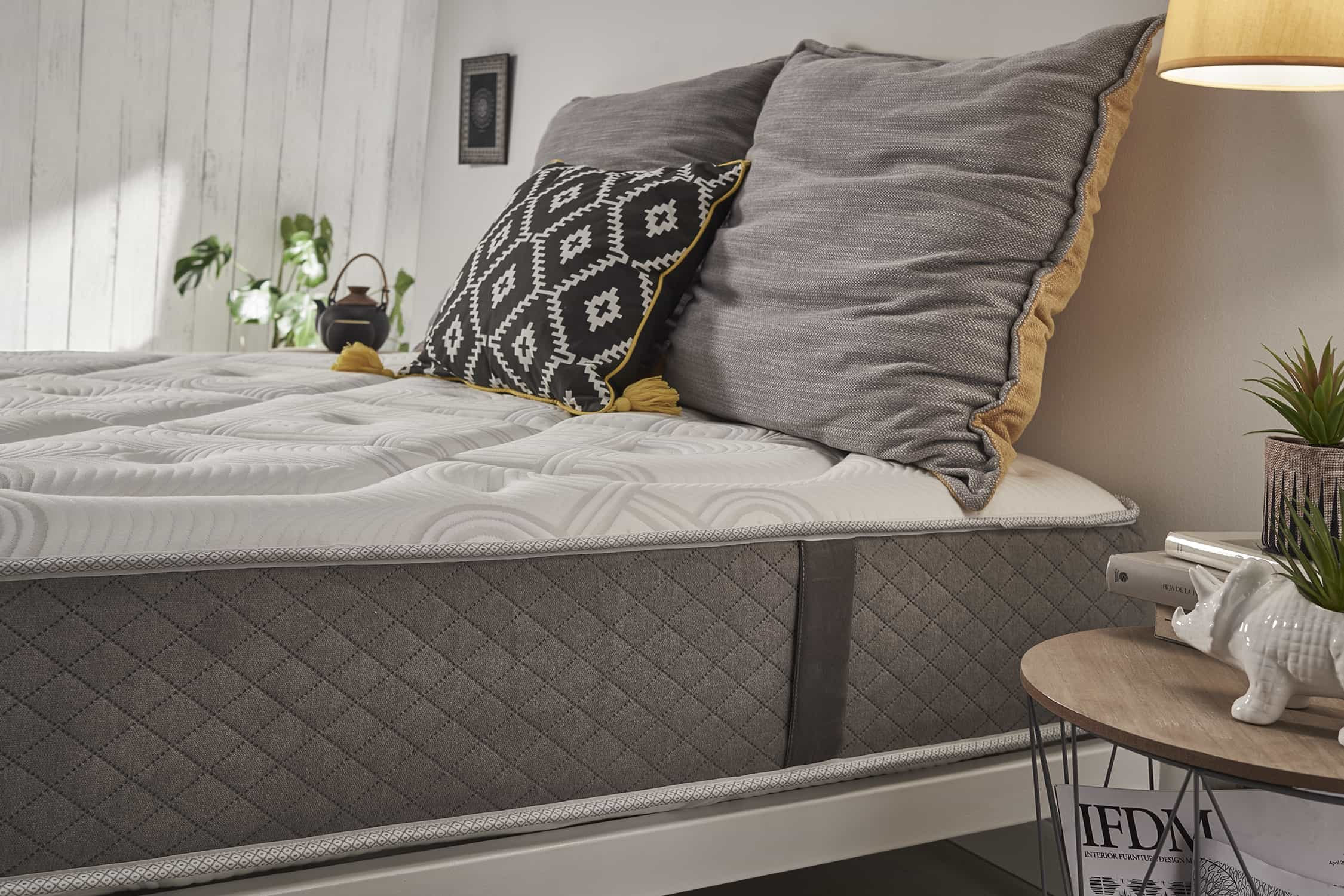 Primer plano de una cama. La cama tiene un cabecero acolchado gris y una cama con fundas y almohadas grises.