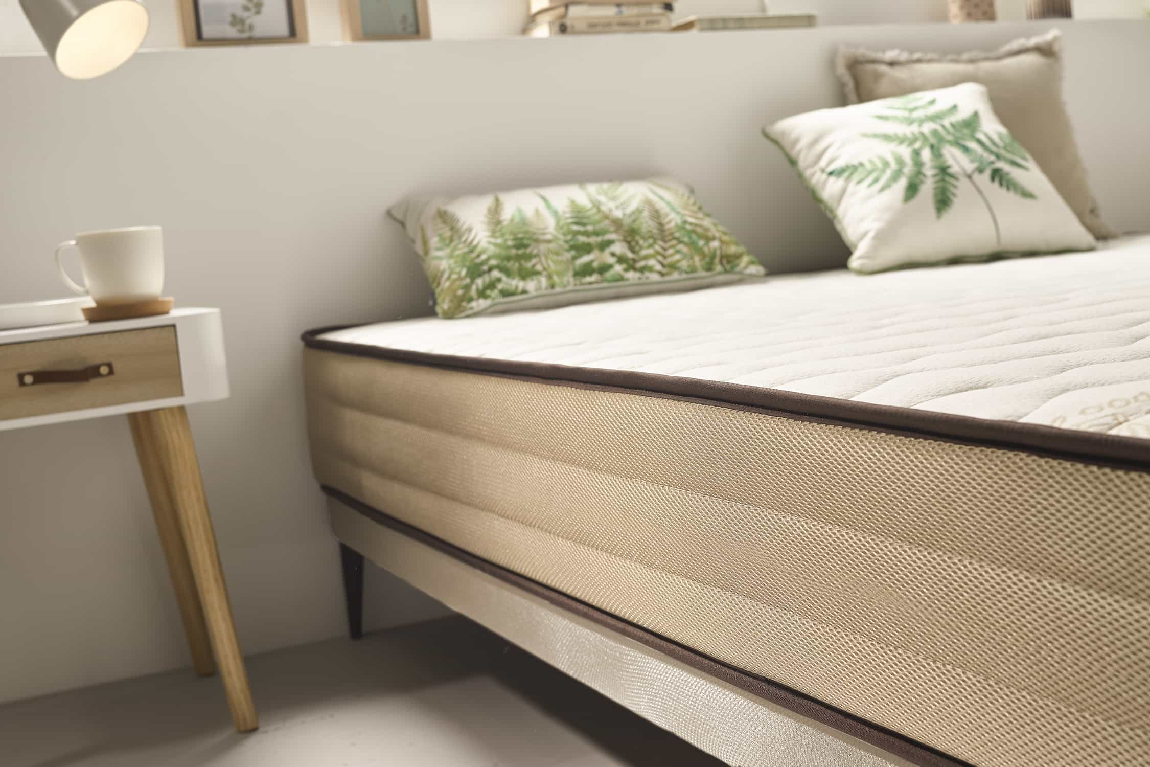 Primer plano de una cama. La cama tiene una parte superior blanca y laterales beige con un borde marrón oscuro y una base beige claro.