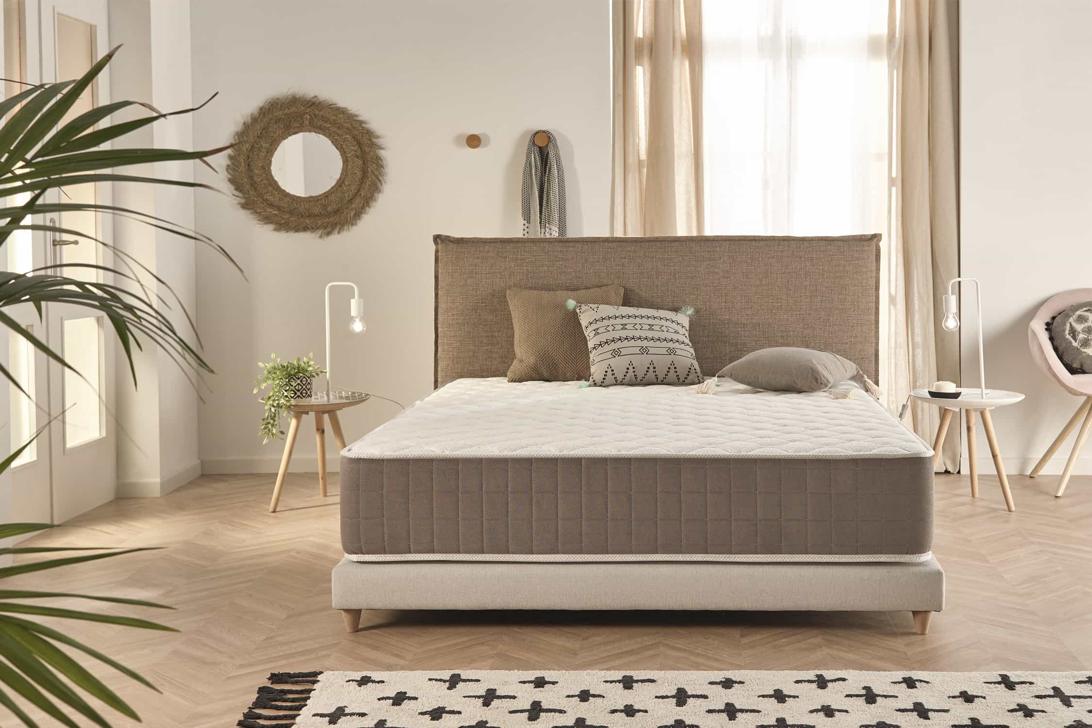 Una cama con colchón de borde marrón, almohadas y una mesita auxiliar con decoración.
