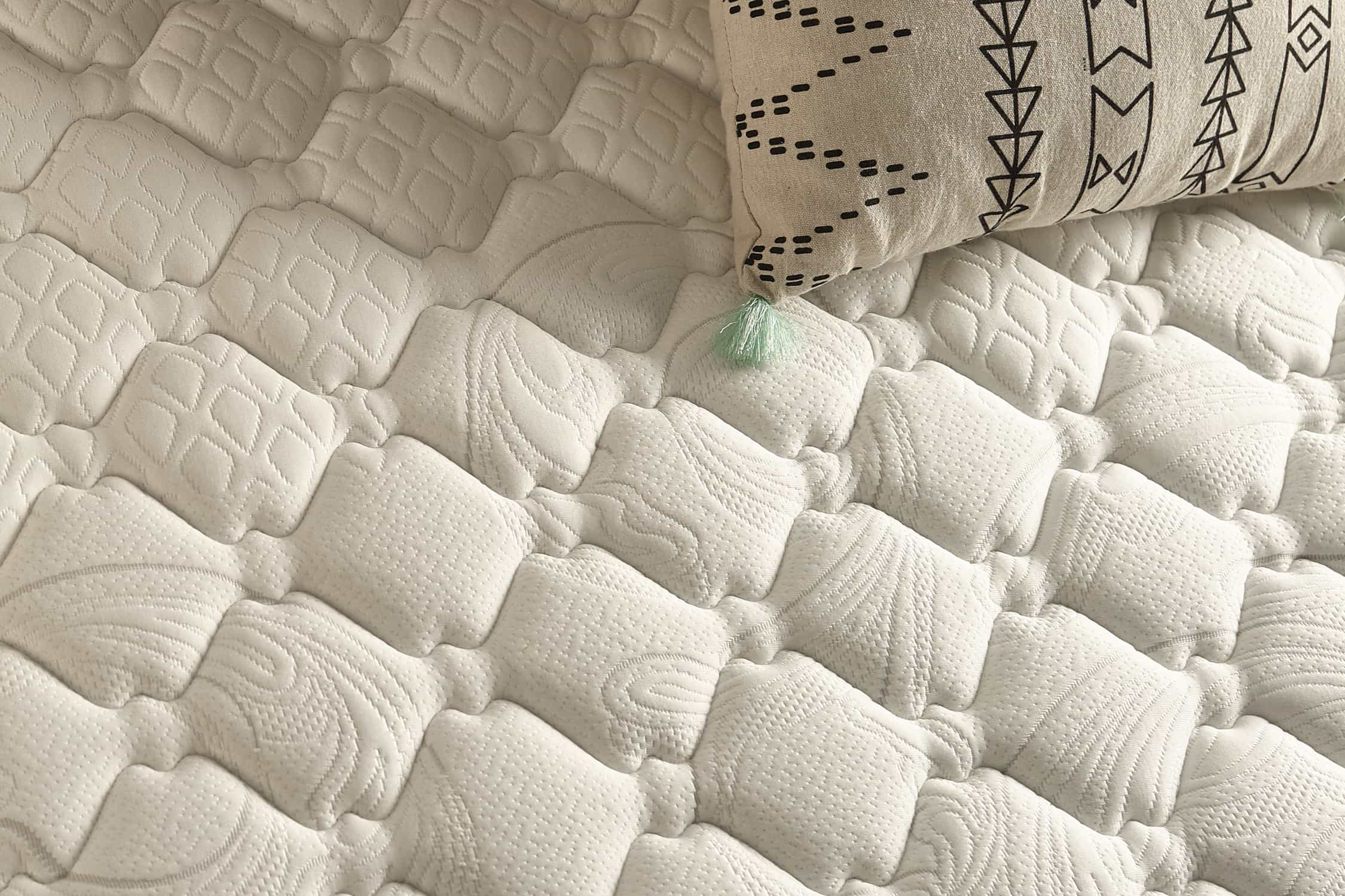 Primer plano de un colchón blanco con textura estampada y una almohada con diseños negros.