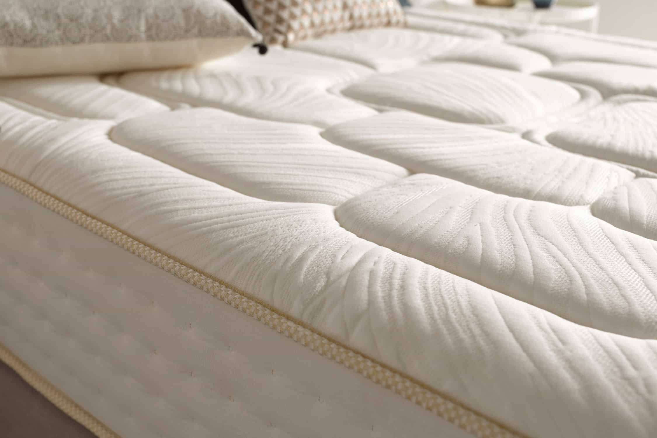 Primer plano de un colchón blanco con un patrón ondulado. Se ve una almohada y una manta en el fondo.