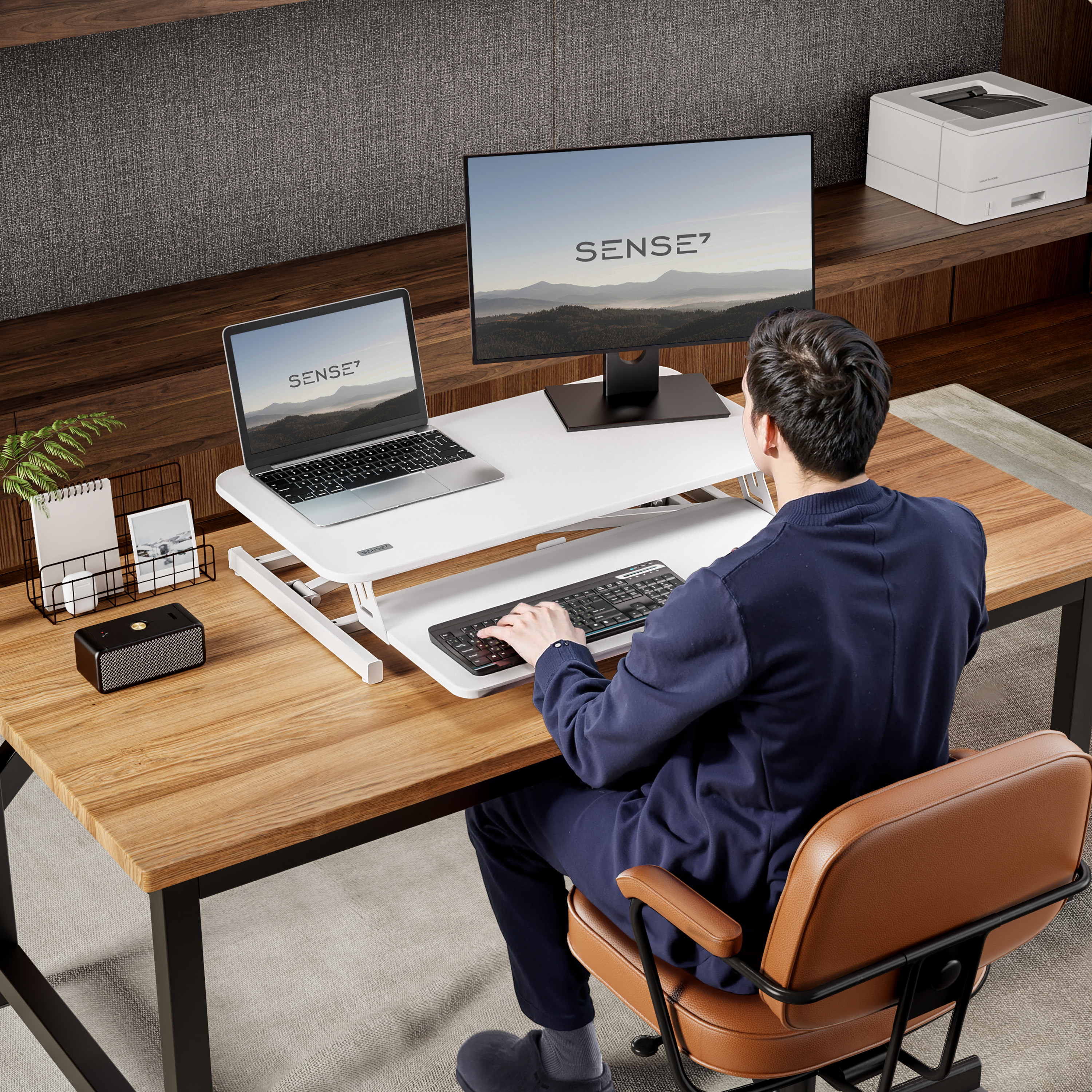 Un hombre trabajando en un portátil y un monitor en un escritorio blanco. Hay una impresora y un altavoz. Configuración de oficina.