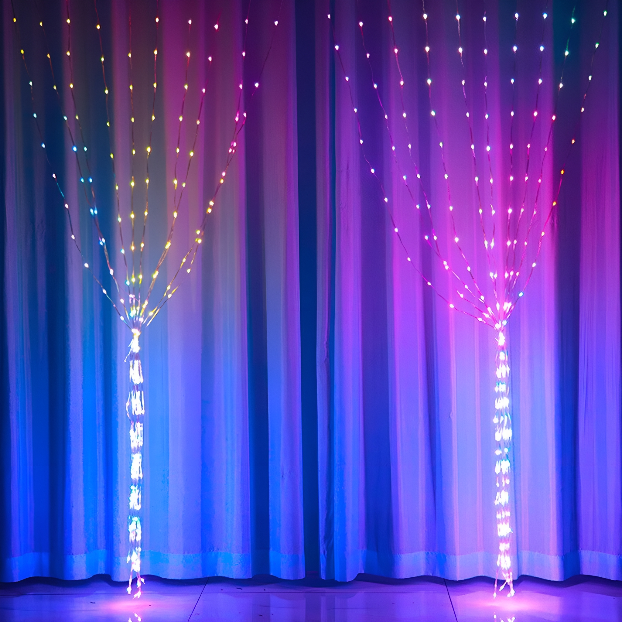 Zwei beleuchtete dekorative LED-Lichtbäume mit bunten Lichtern vor Vorhang.