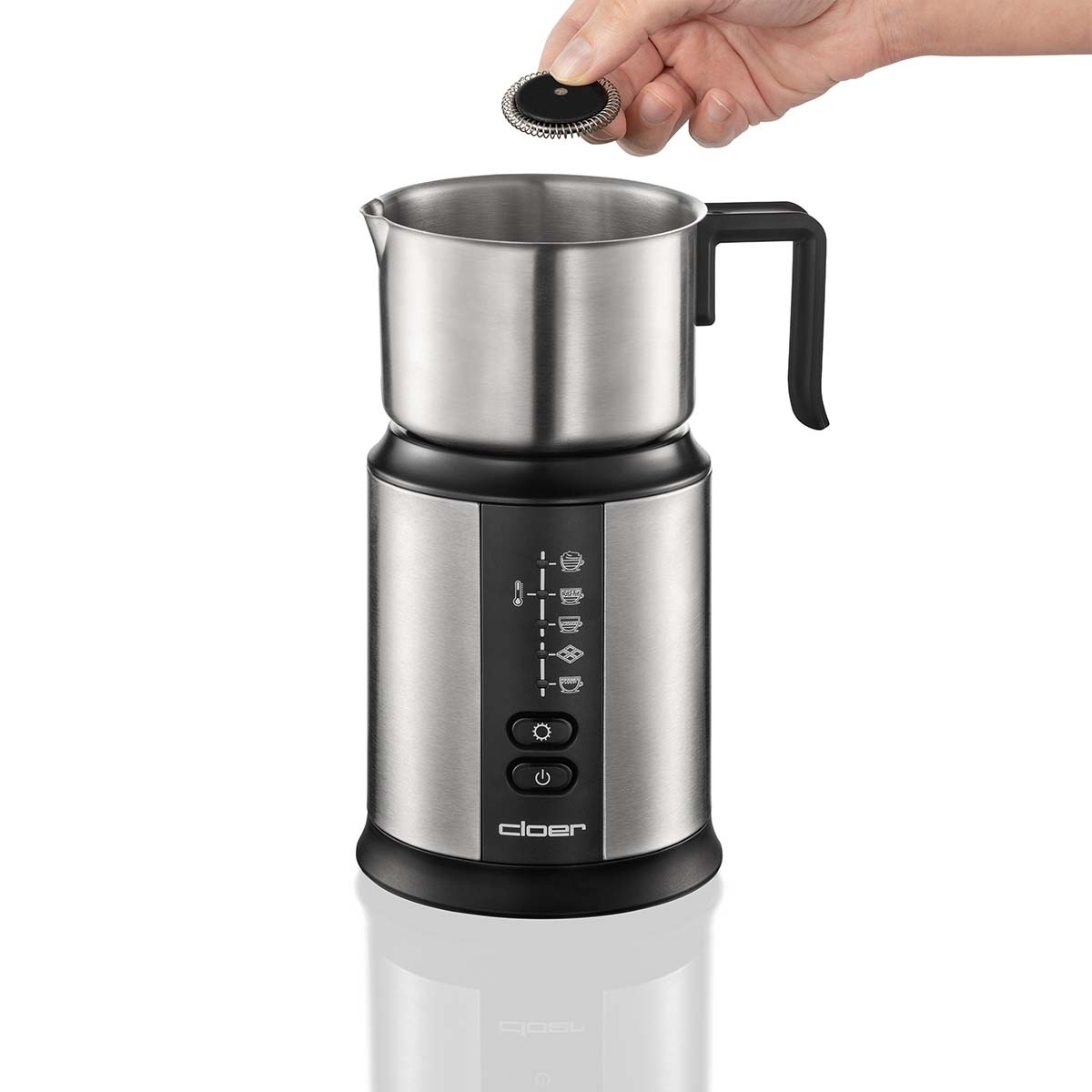 Srebrny spieniacz do mleka na czarnej podstawie. Ręka trzyma przystawkę do spieniania. Marka: 'cloer'.