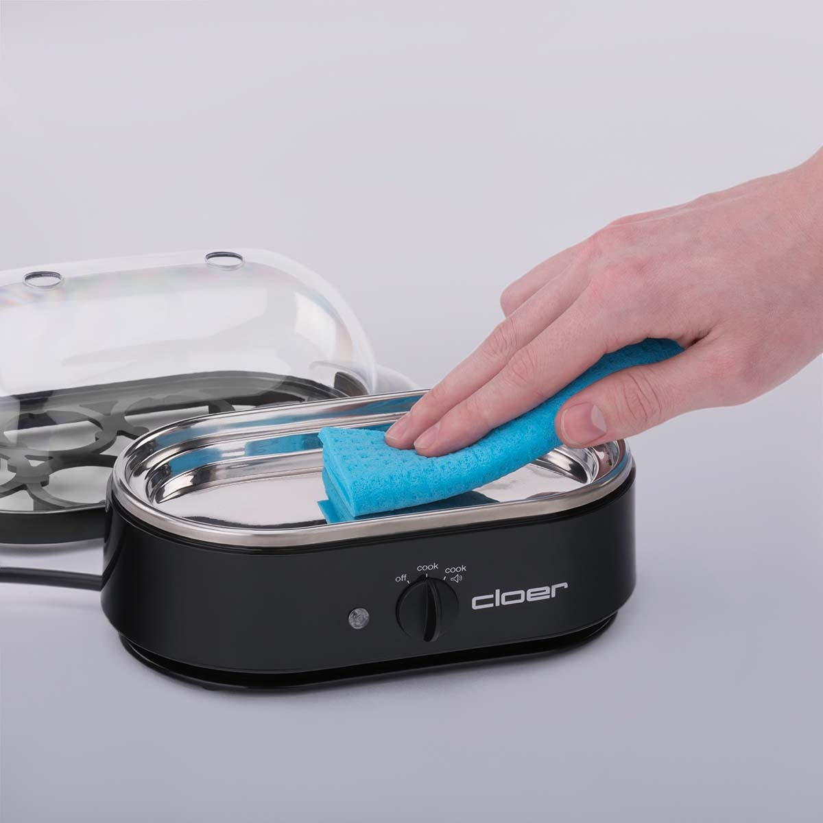 Ręka czyszcząca garnek do jajek. Garnek jest otwarty z niebieską gąbką.