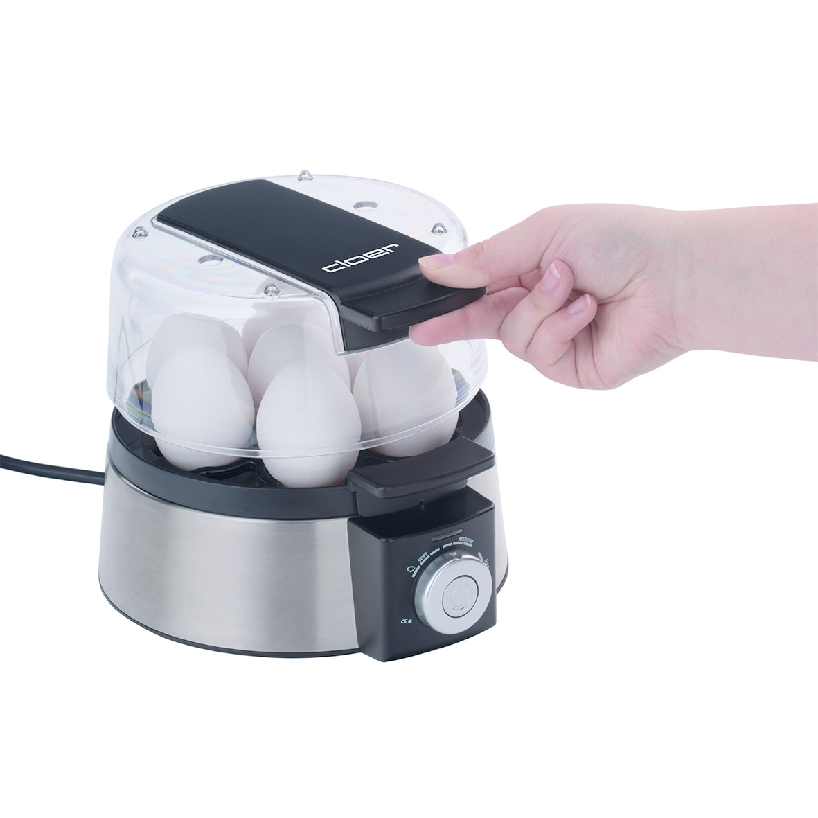 Ręka zamyka pokrywę urządzenia do gotowania jajek. Urządzenie jest czarno-srebrne, z pokrętłem. W środku są jajka.