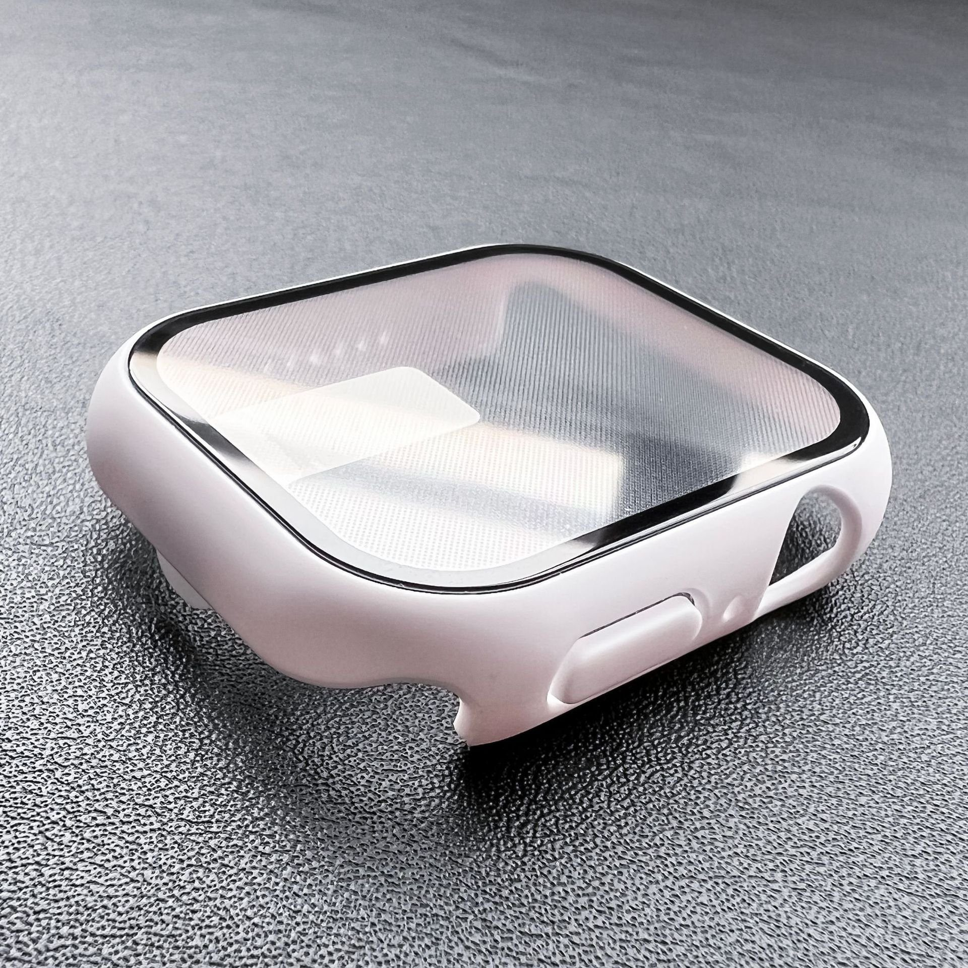 Weißes Apple Watch-Gehäuse mit klarem Displayschutz. Das Gehäuse liegt auf einer dunklen, strukturierten Oberfläche. Rückseite mit Knopf.