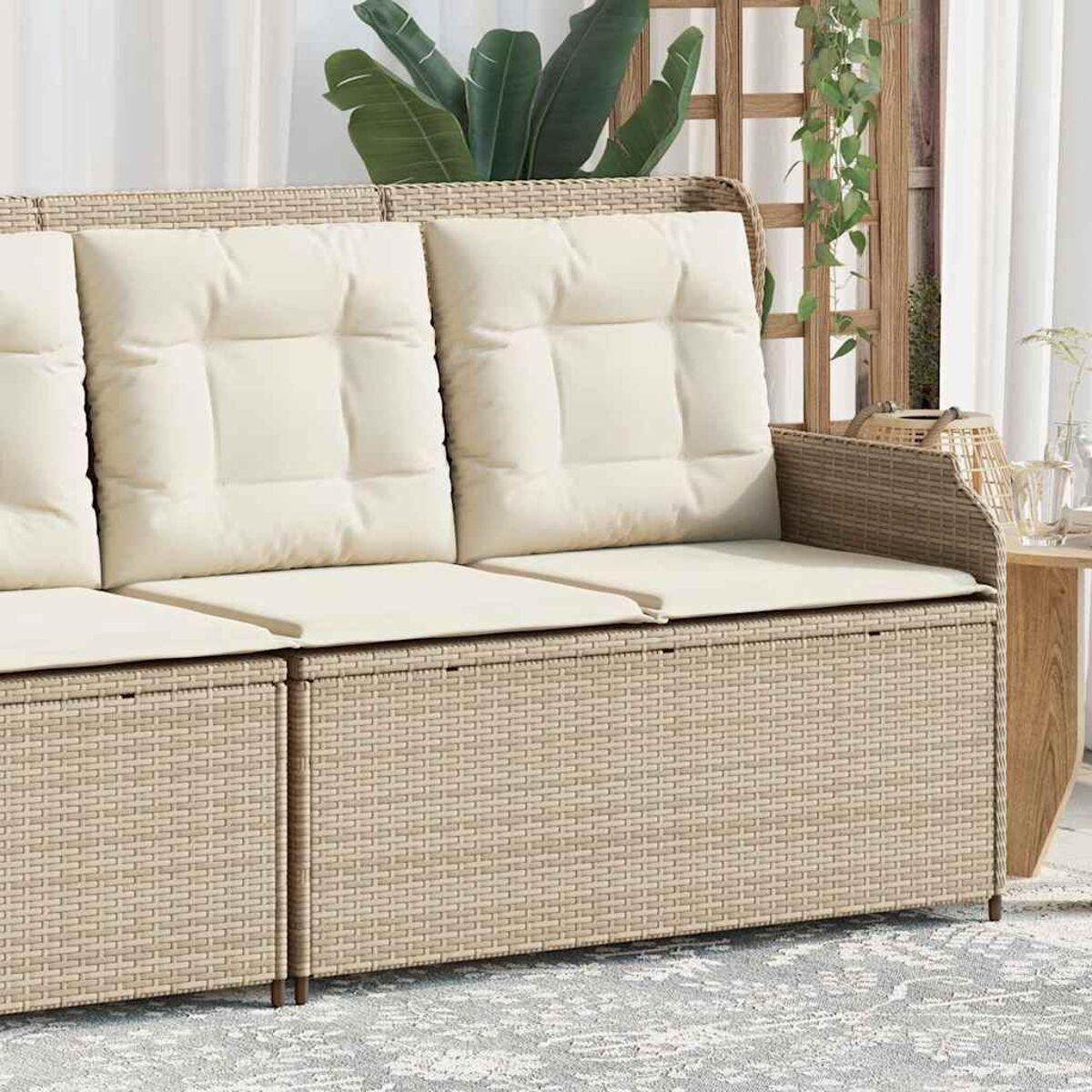 Beiges Rattansofa mit drei cremefarbenen Kissen. Im Hintergrund ein Fenster und Pflanzen.