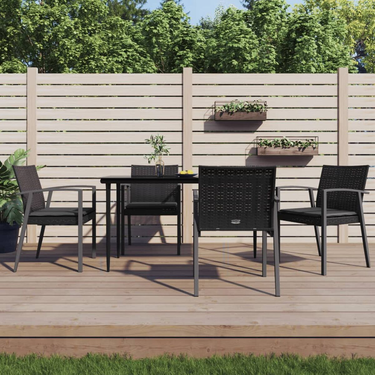 Essgruppe im Freien auf einer Holzterrasse. Schwarze Stühle um einen Tisch, grüner Hintergrund.