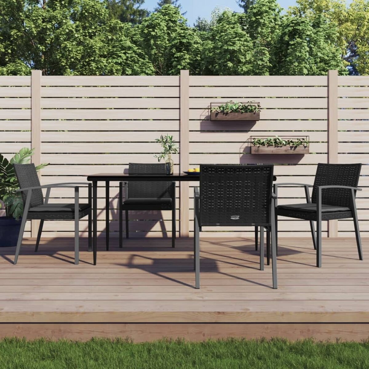 Essgruppe im Freien mit schwarzen Stühlen und Tisch auf Holzterrasse, Zaun und Pflanzen.