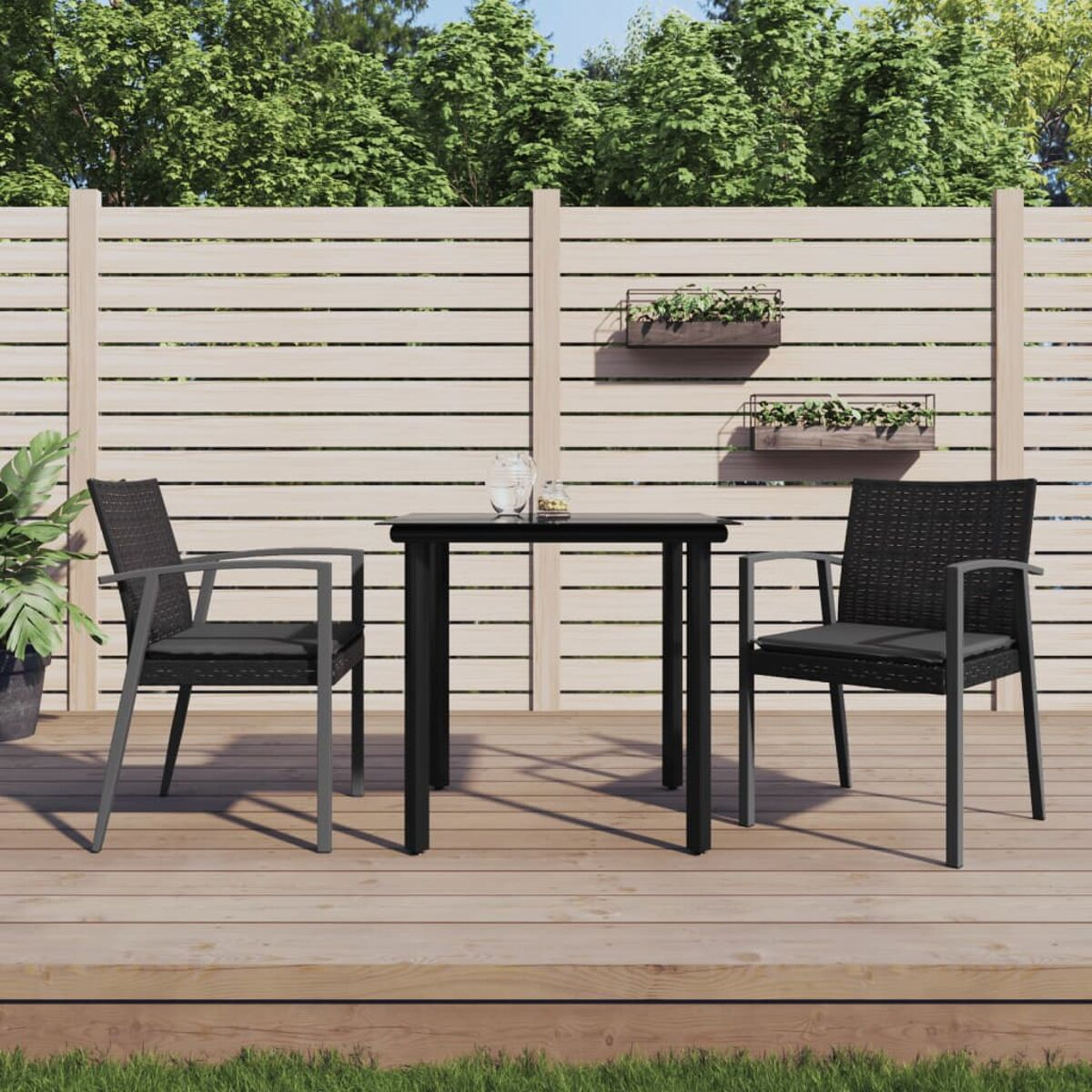 Tisch, zwei Stühle auf der Terrasse, Zaun und Bäume im Hintergrund.