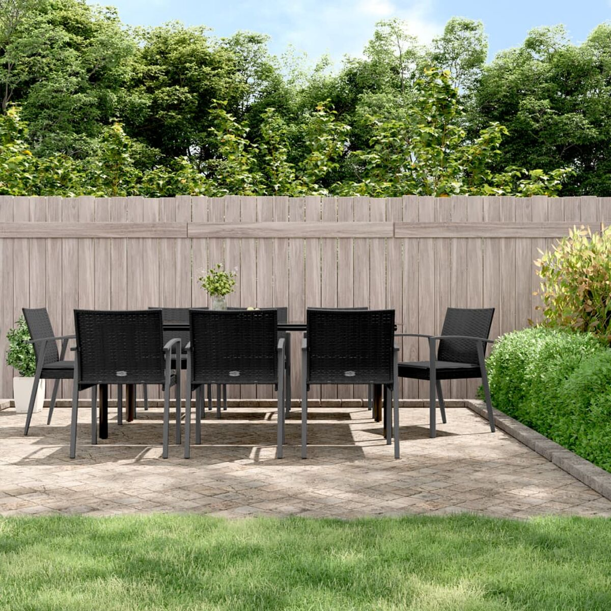 Terrassenset: schwarzer Tisch, Stühle, grünes Gras, Stein-Patio, Holzzaun und Bäume.