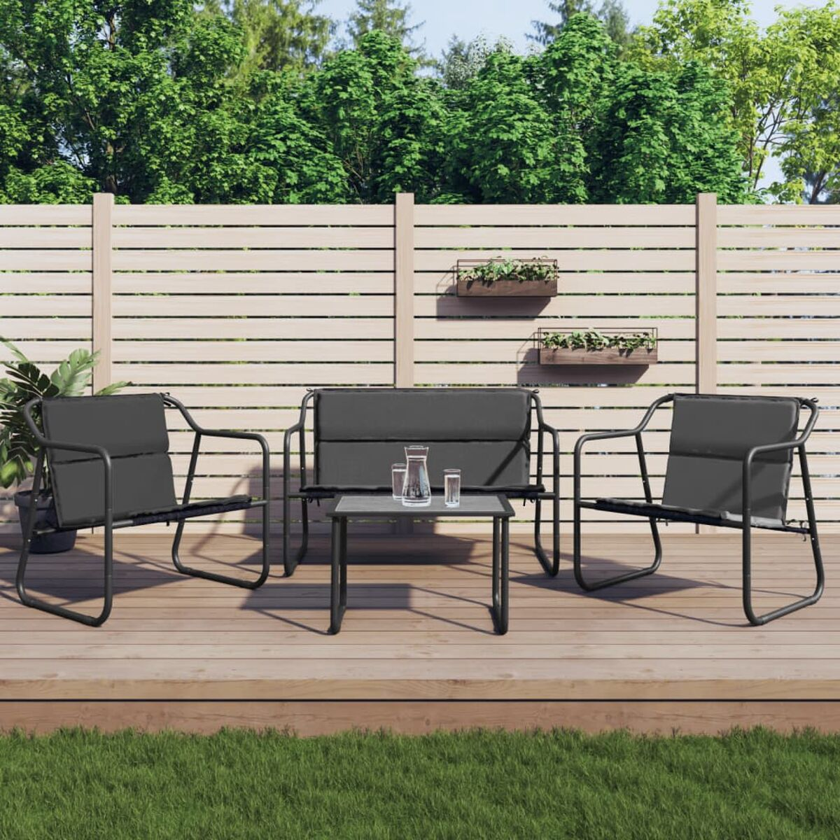 Ein Terrassenset: zwei Stühle, ein Sofa und ein Tisch auf einem Holzdeck. Pflanzen im Hintergrund.