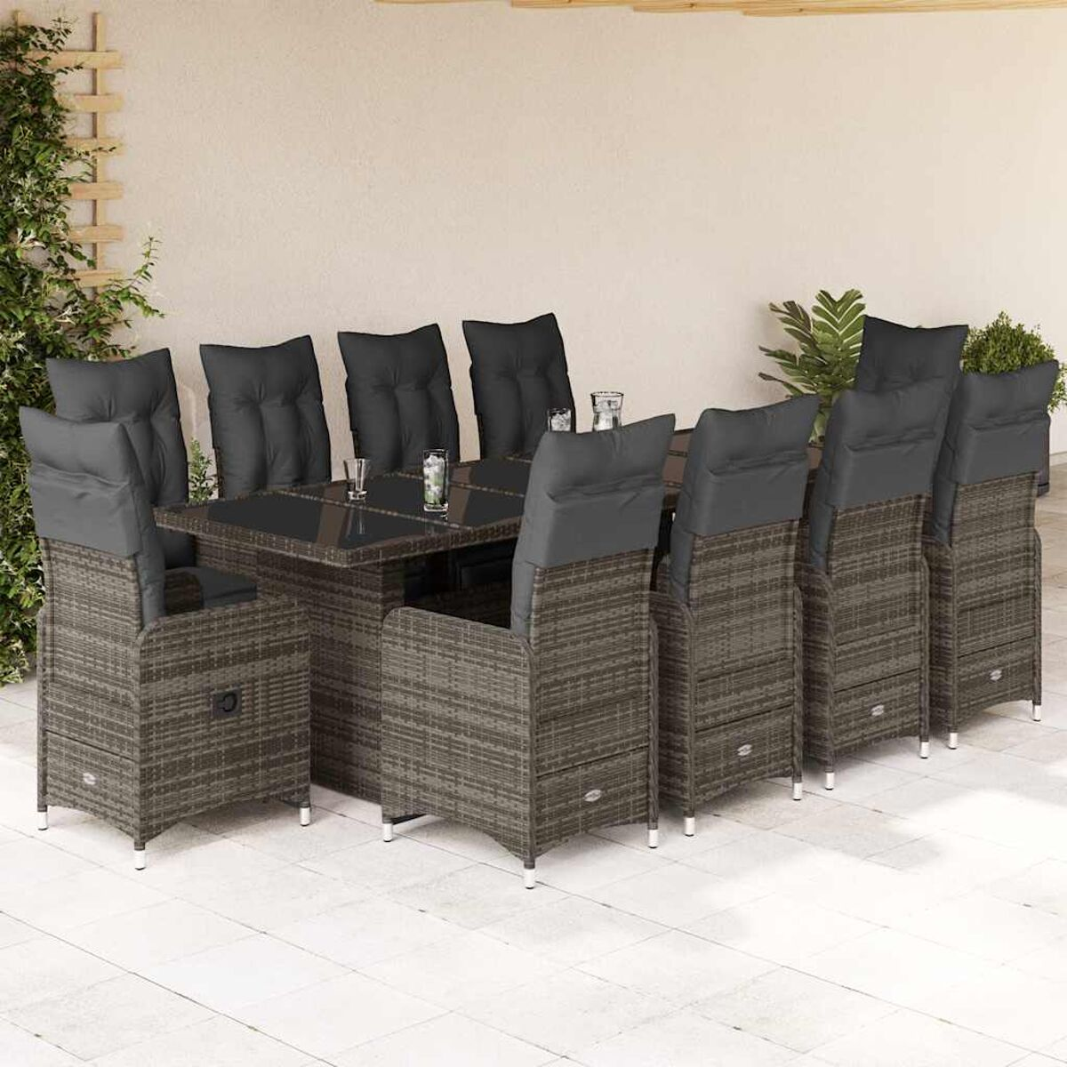 Set da pranzo all'aperto: tavolo, 8 sedie con cuscini. Vimini grigio, cuscini neri. Sfondo muro beige.