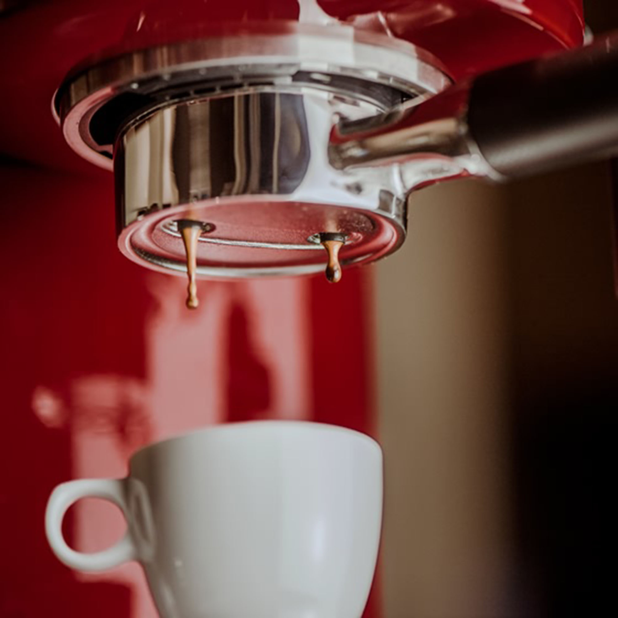 Espressomaschine mit Kaffee, der in eine weiße Tasse tropft. Rote Maschine mit geringer Tiefenschärfe.