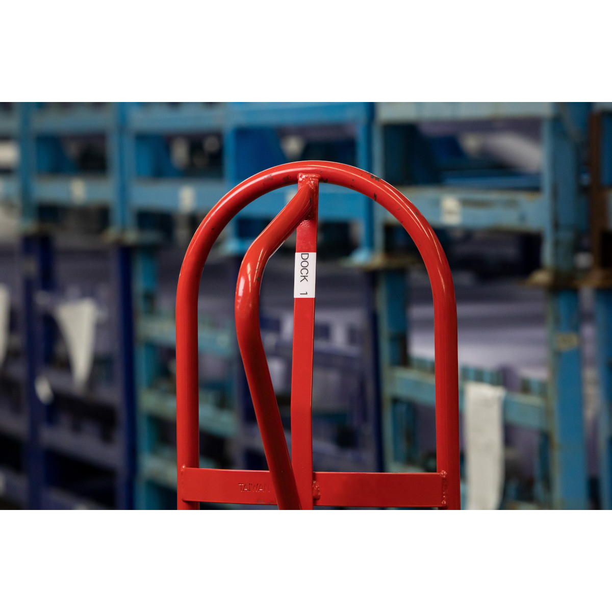 Carrello rosso con etichetta bianca. Scaffalature blu sullo sfondo sfocato.