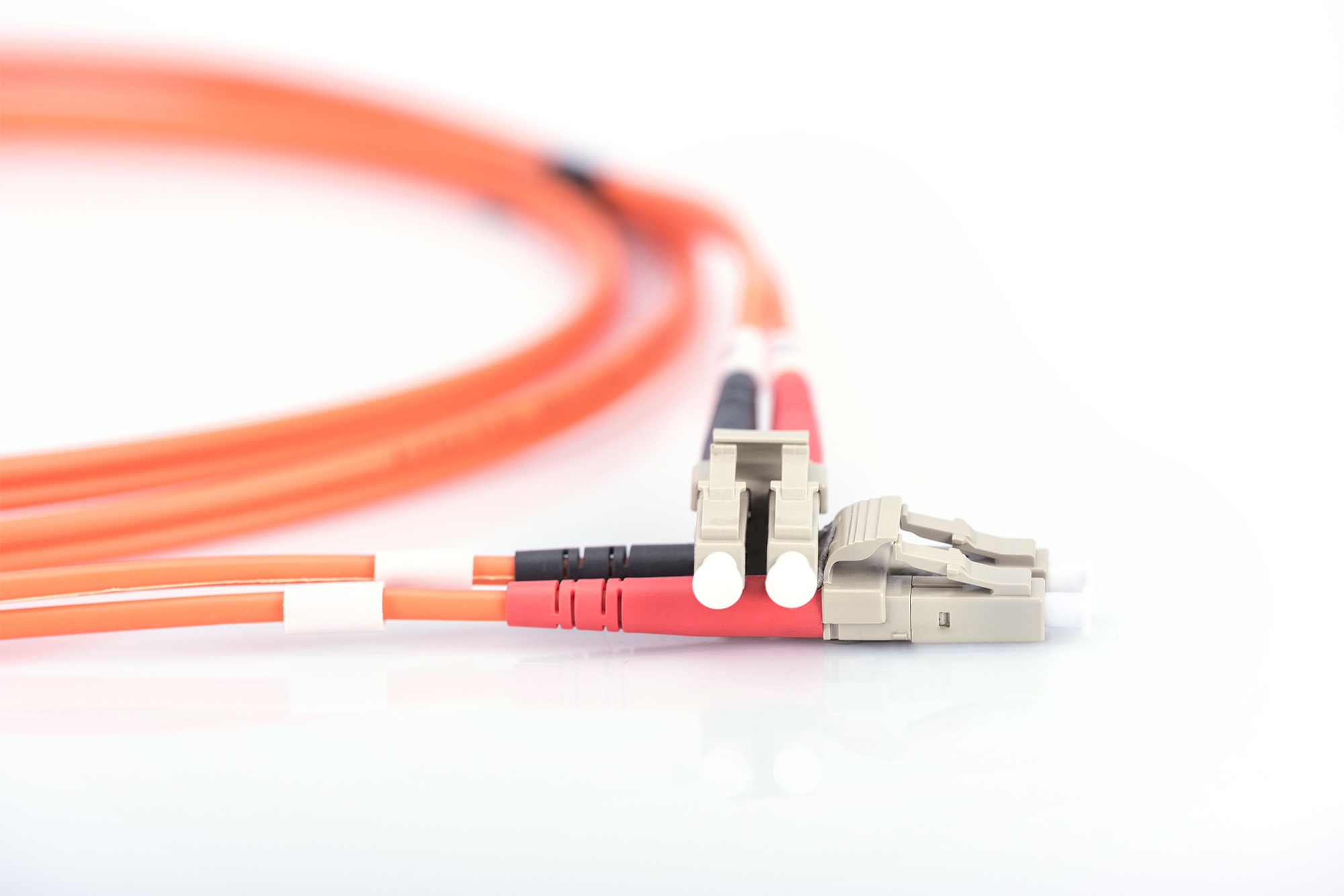 Due cavi in fibra ottica arancioni con strisce bianche e rosse e connettori colorati chiari su una superficie bianca.
