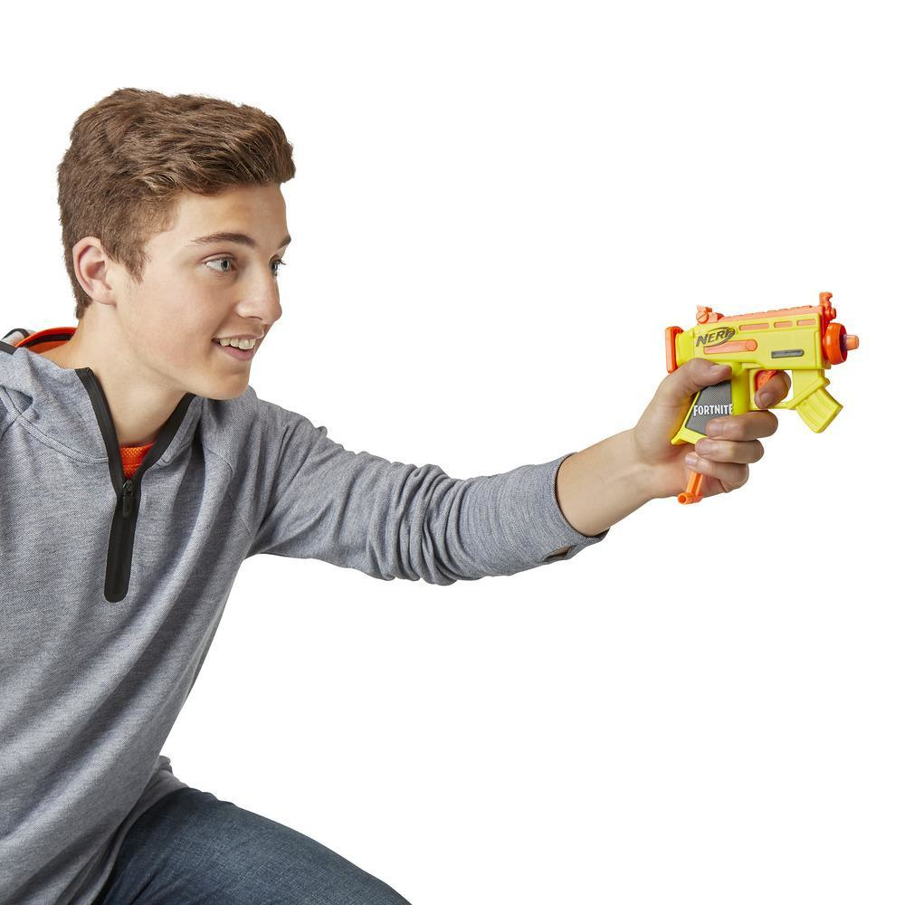 Ein junger Mann hält eine gelbe und orangefarbene Nerf Fortnite-Pistole und zielt damit. Er lächelt.