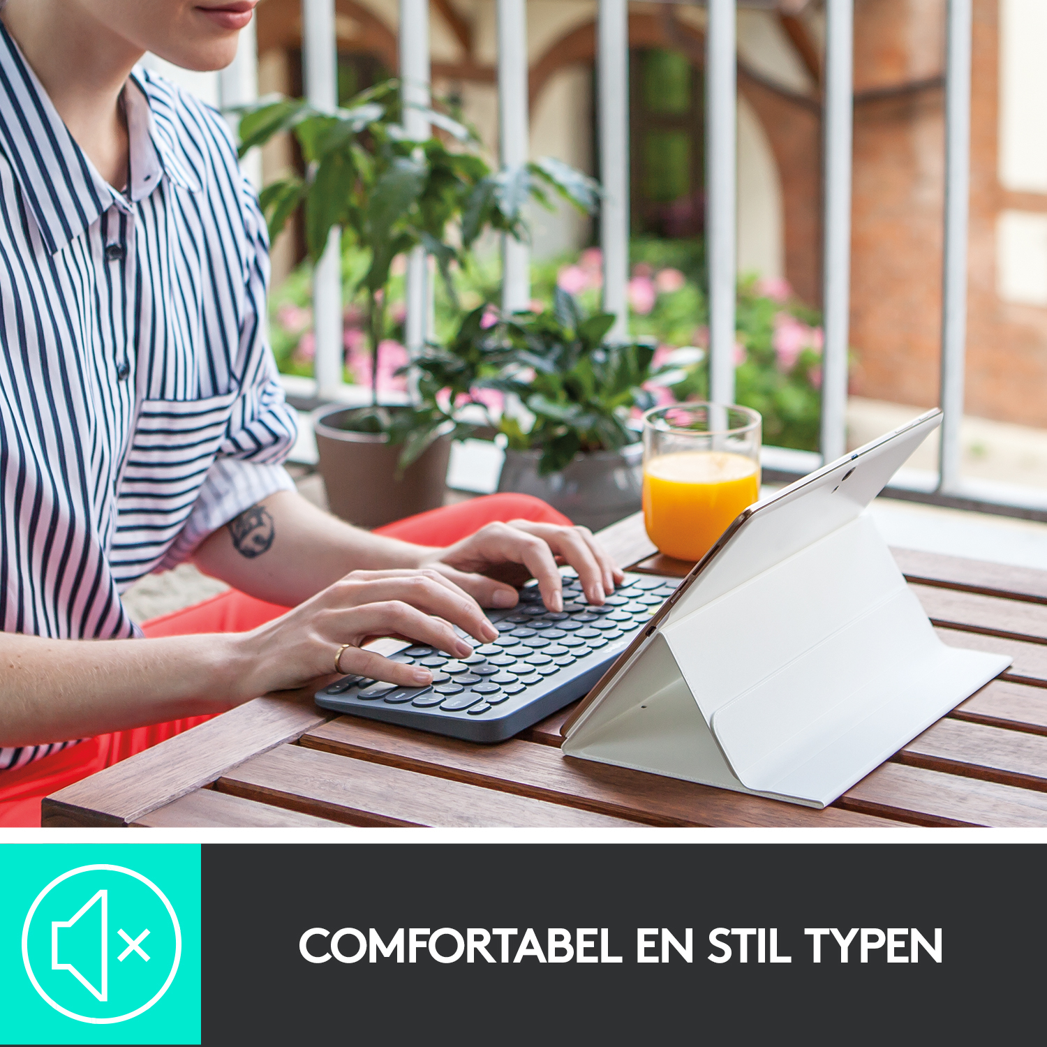 Vrouw typt op tablet met aangesloten toetsenbord. Glas sap op tafel. Achtergrond van balkon met planten.