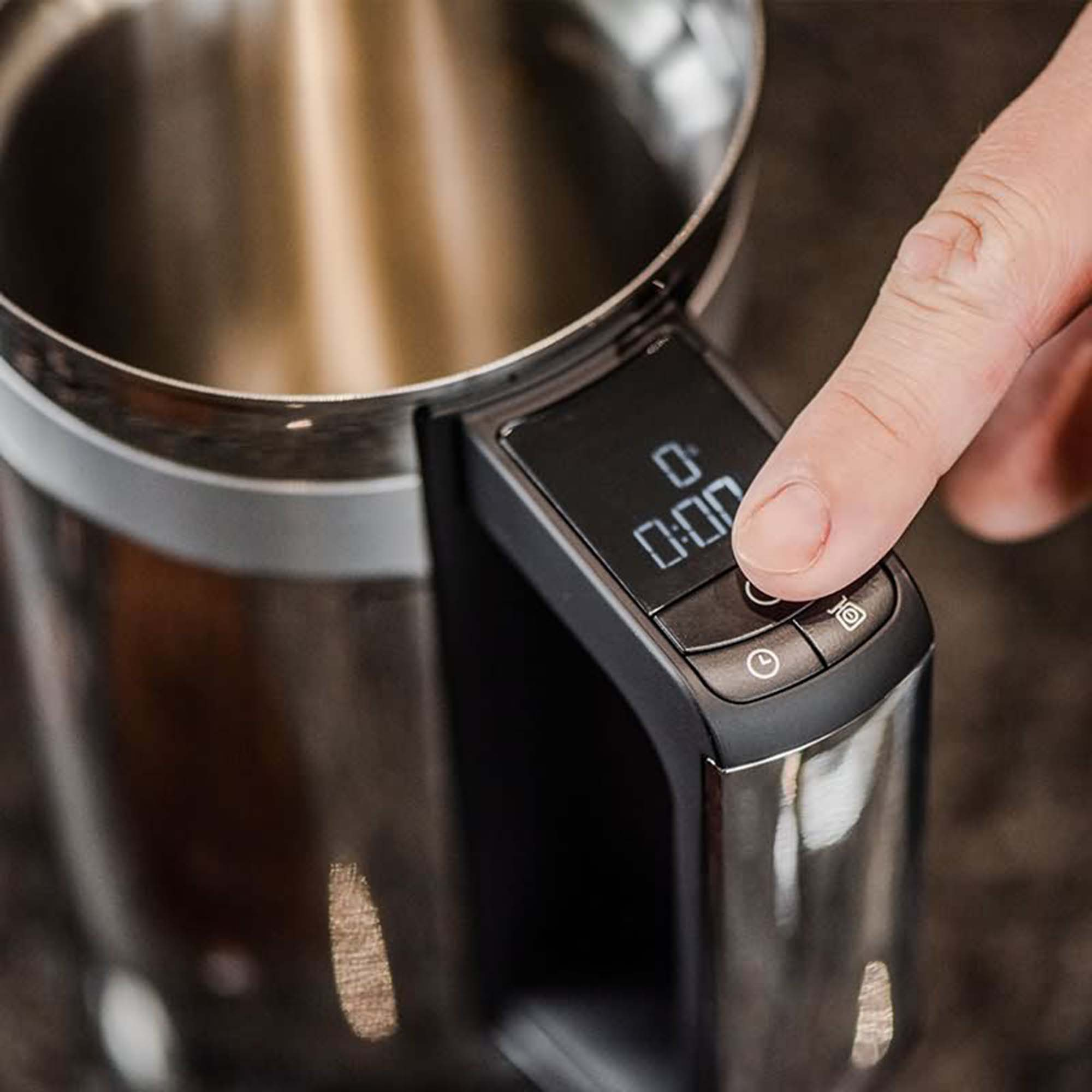 Hand drückt Knopf auf einem schwarzen und silbernen Kaffeezubereiter.