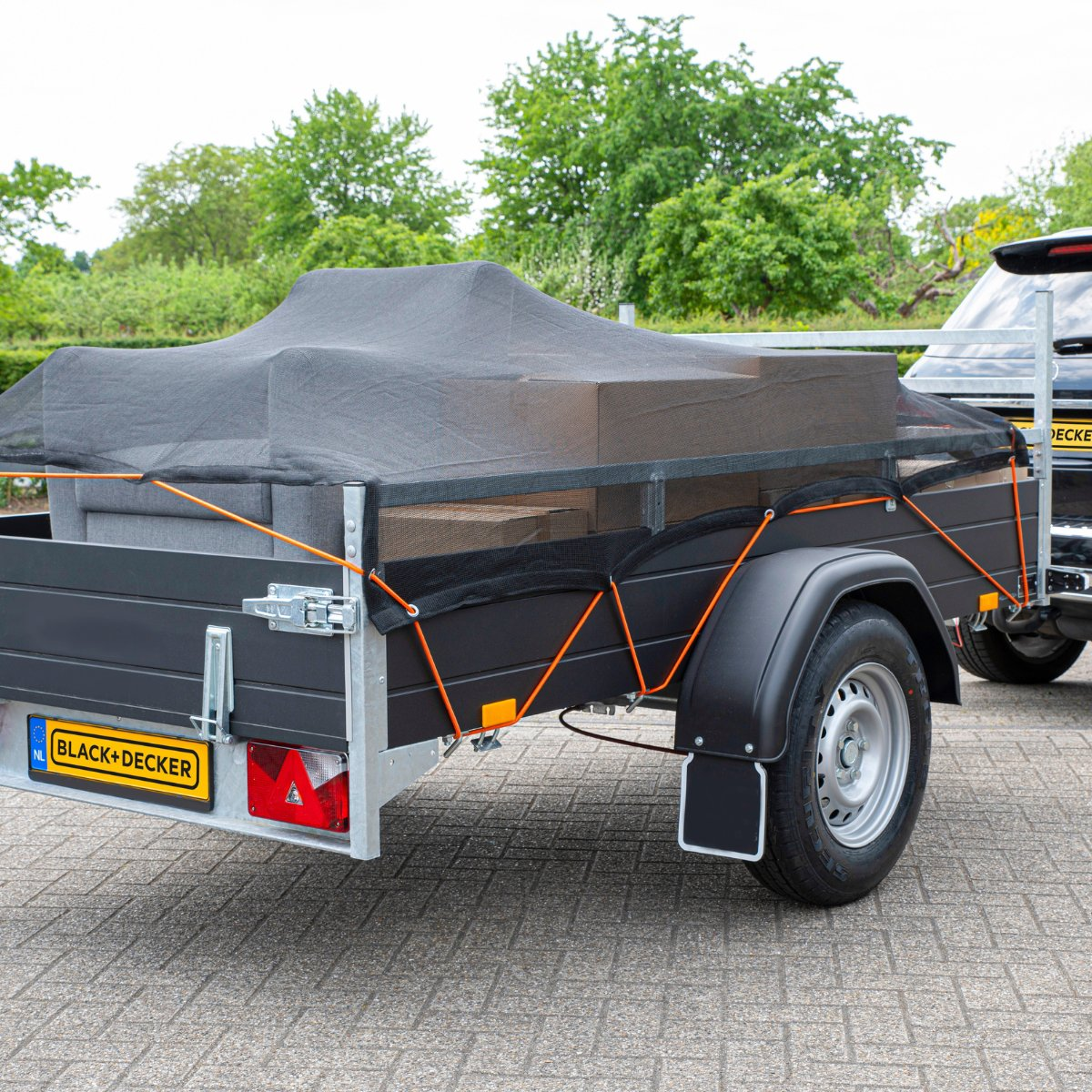 Zwarte aanhanger met afgedekte lading en oranje riemen, verbonden met een zwarte auto.