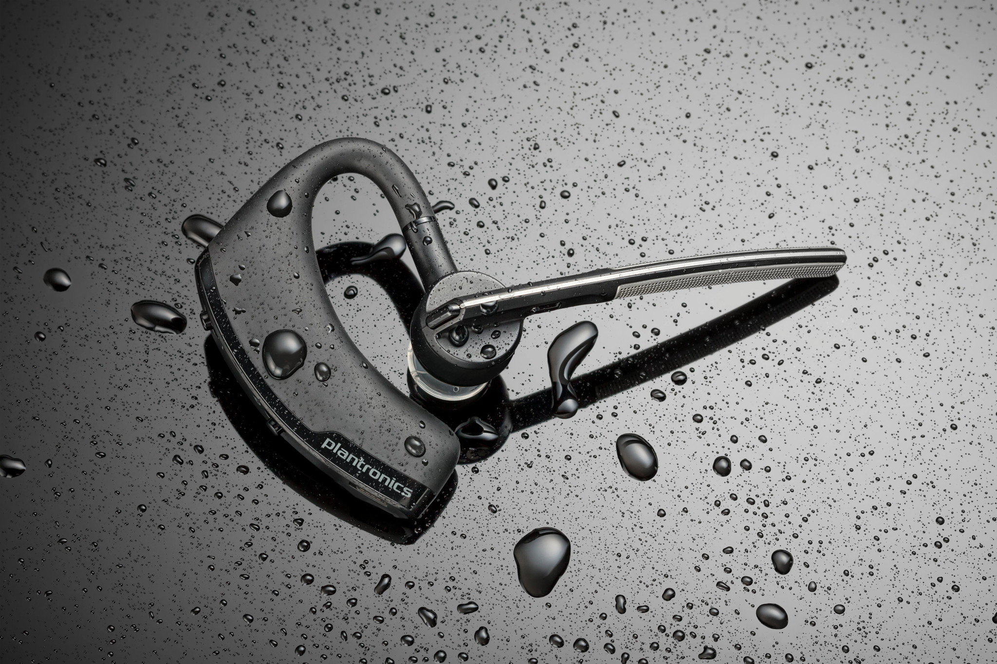 Cuffia Bluetooth nera con gocce d'acqua, su una superficie bagnata.