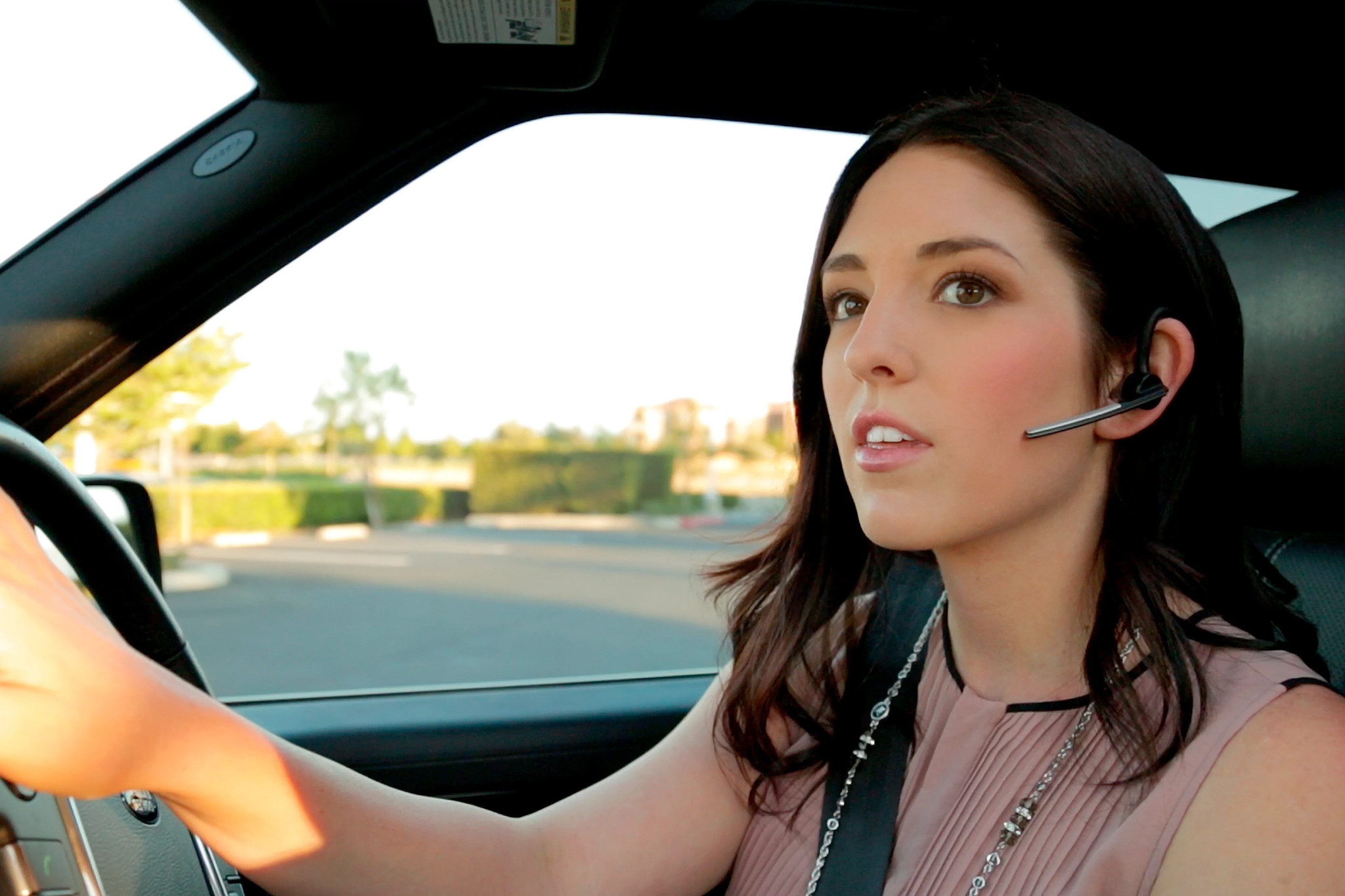 Donna guida un'auto, indossa un auricolare Bluetooth, concentrata.