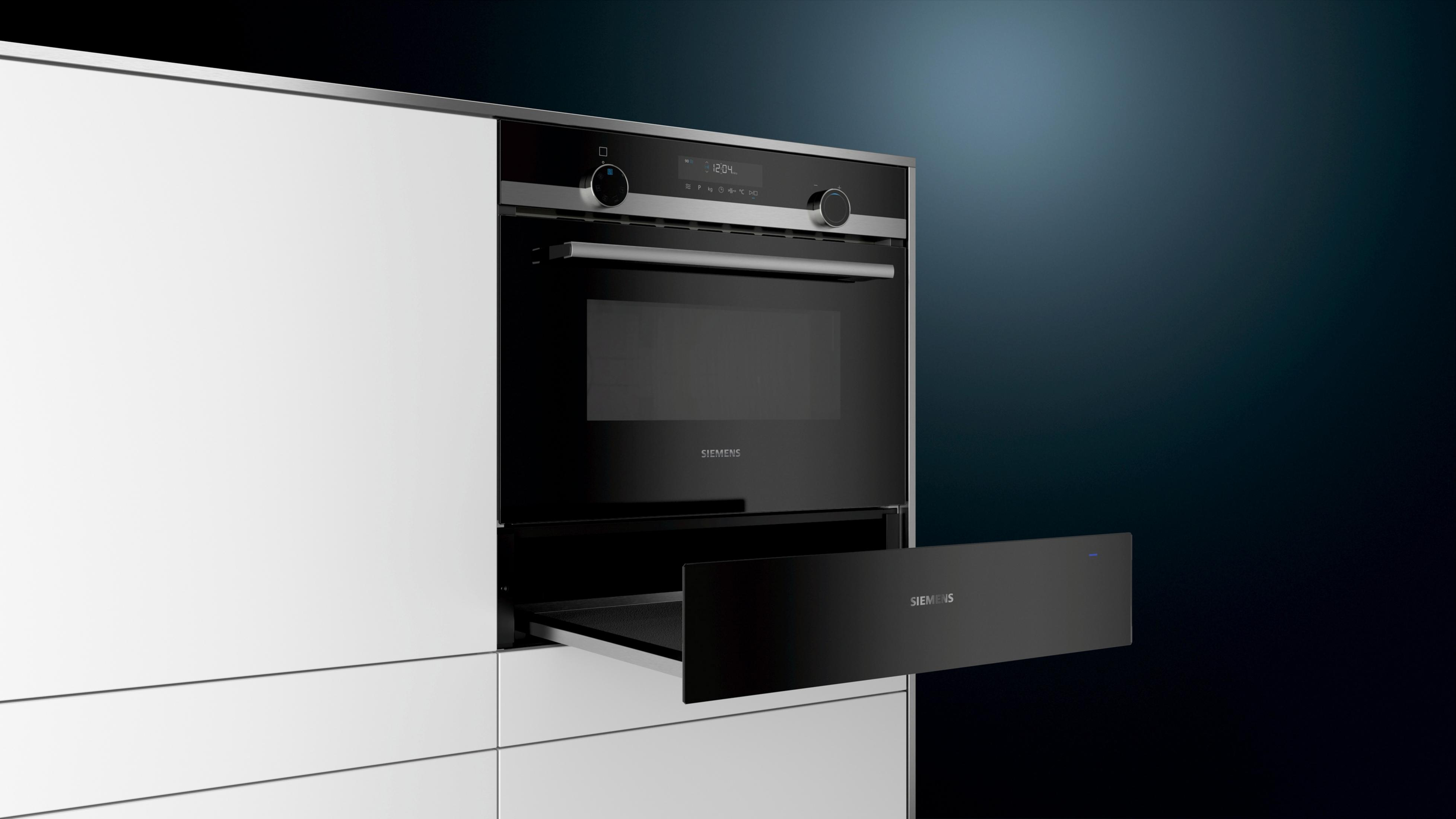 Forno nero moderno con cassetto aperto, installato in un mobile da cucina bianco. Sfondo sfumato blu scuro.