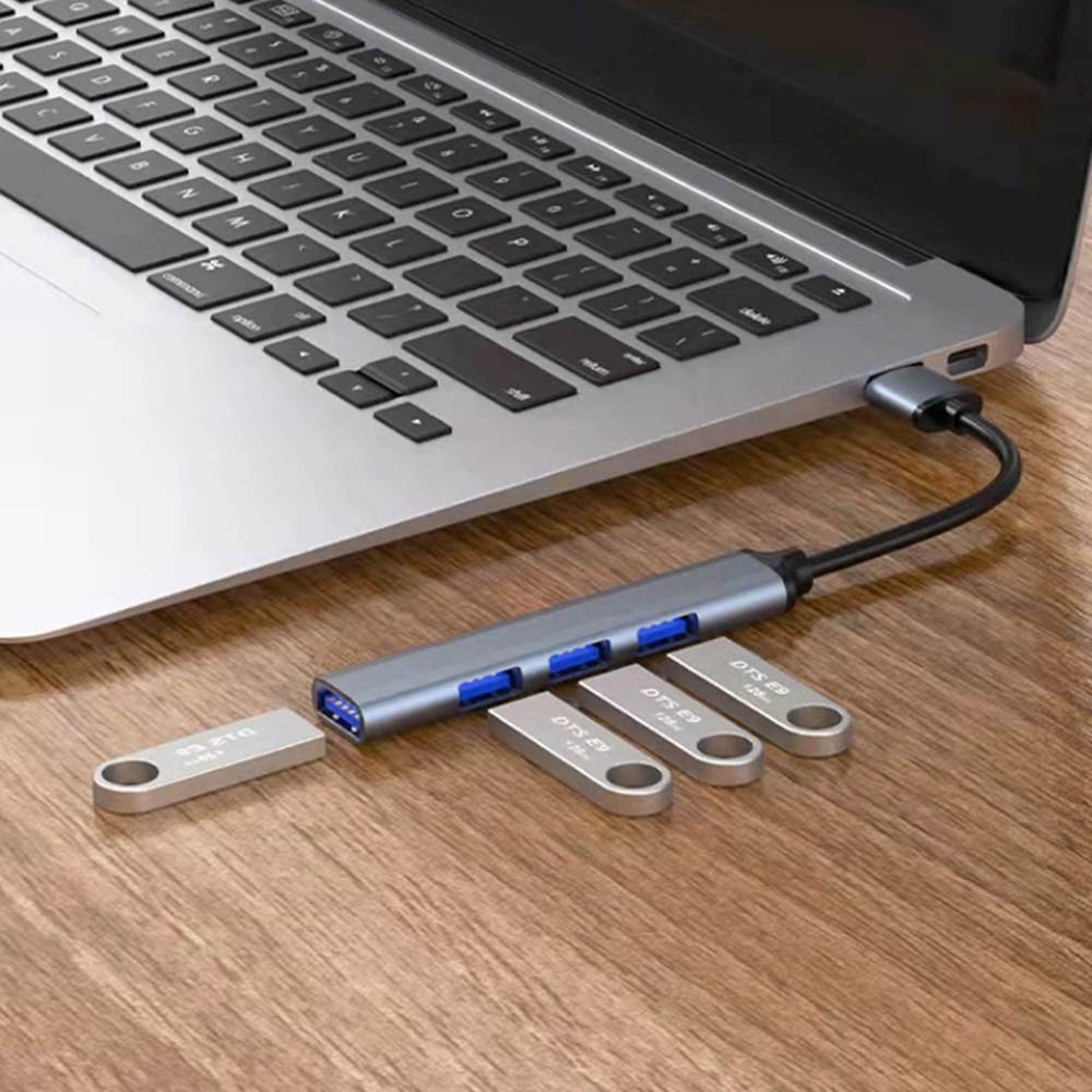 Ein USB-Hub ist mit einem Laptop verbunden, daneben befinden sich USB-Sticks auf einer Holzoberfläche.
