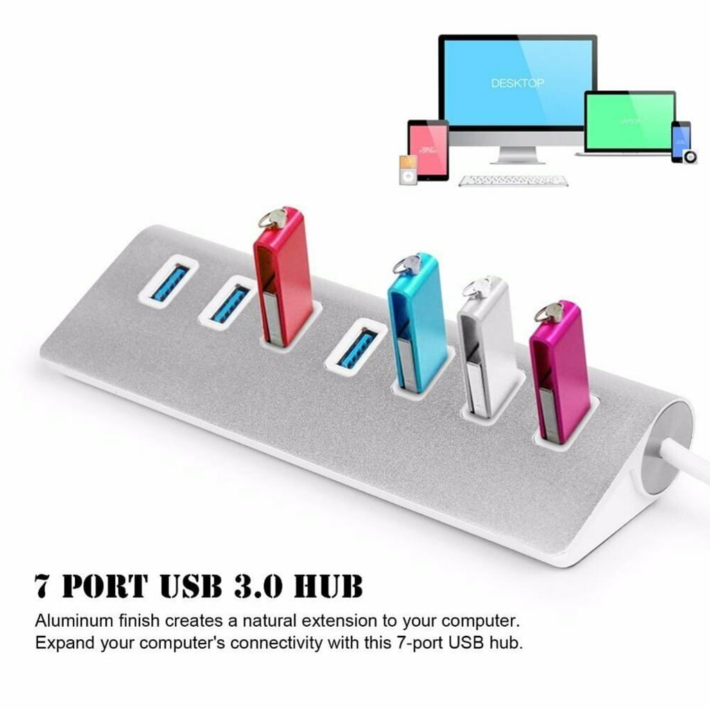 USB-Hub mit sieben Anschlüssen. Bunte USB-Laufwerke eingesteckt. Desktop mit Monitoren und Geräten im Hintergrund.