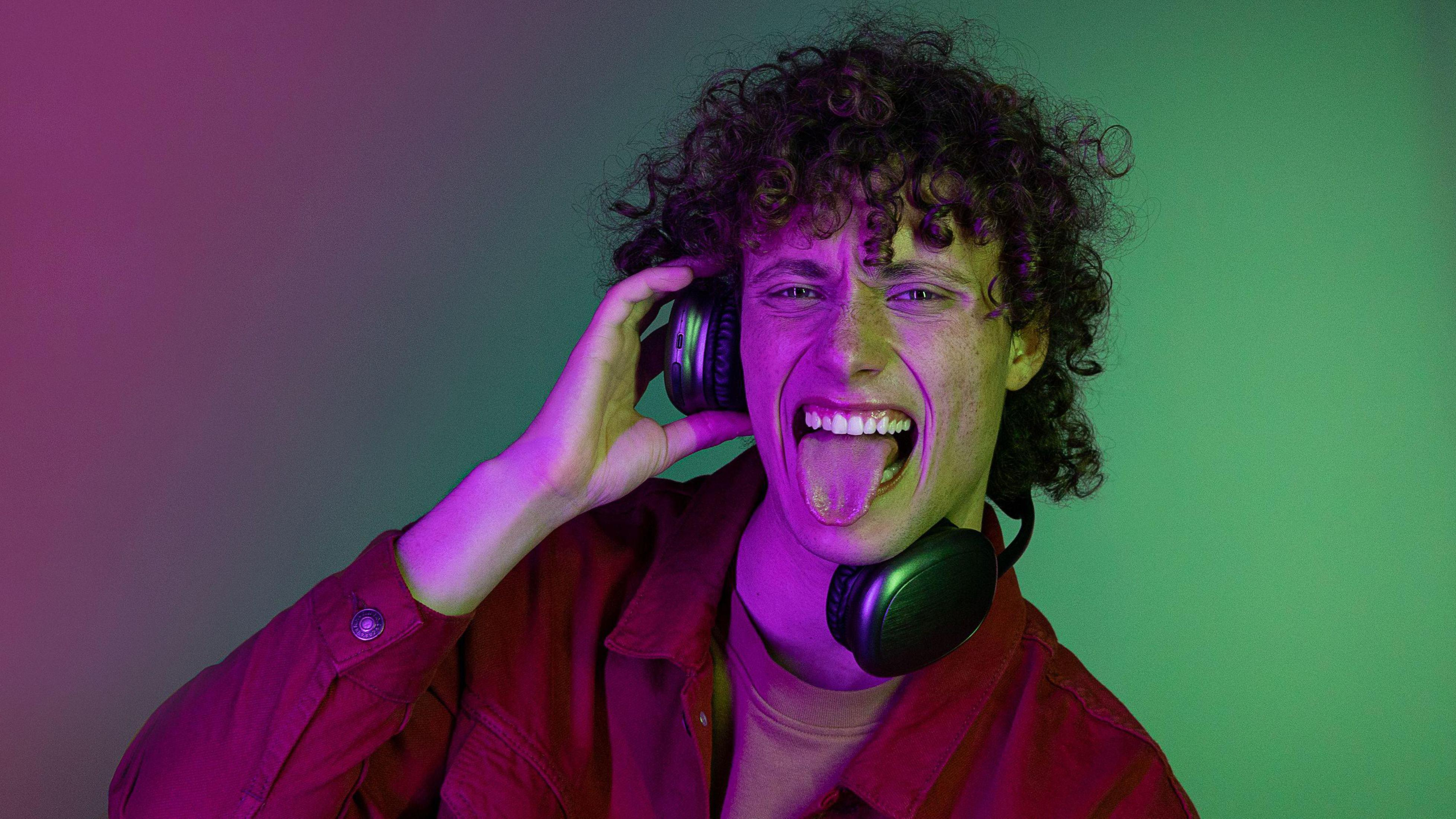 Mężczyzna z kręconymi włosami wystawiający język, w słuchawkach.