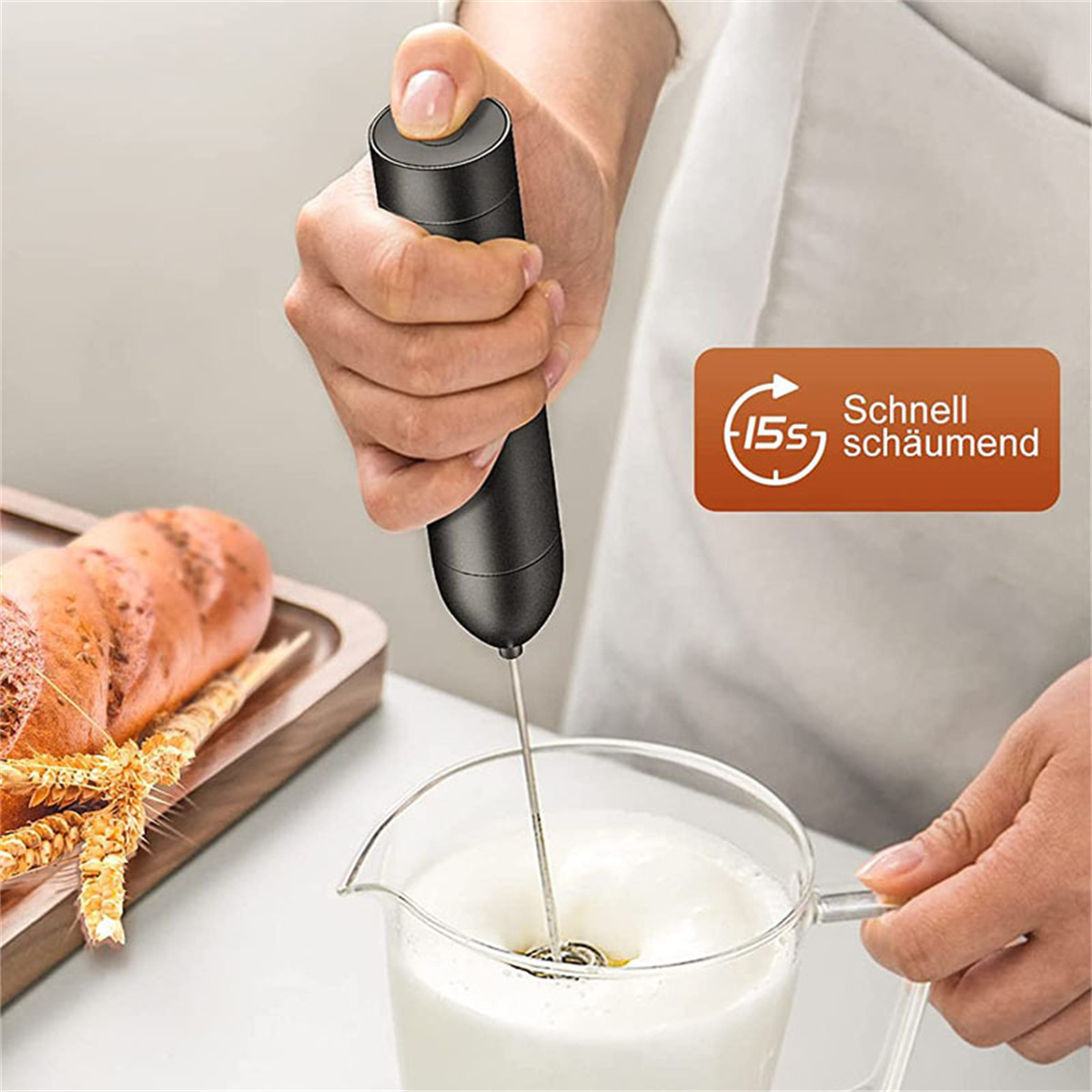 Hand, die einen schwarzen Milchaufschäumer verwendet, um Milch in einen Glasbecher aufzuschäumen.