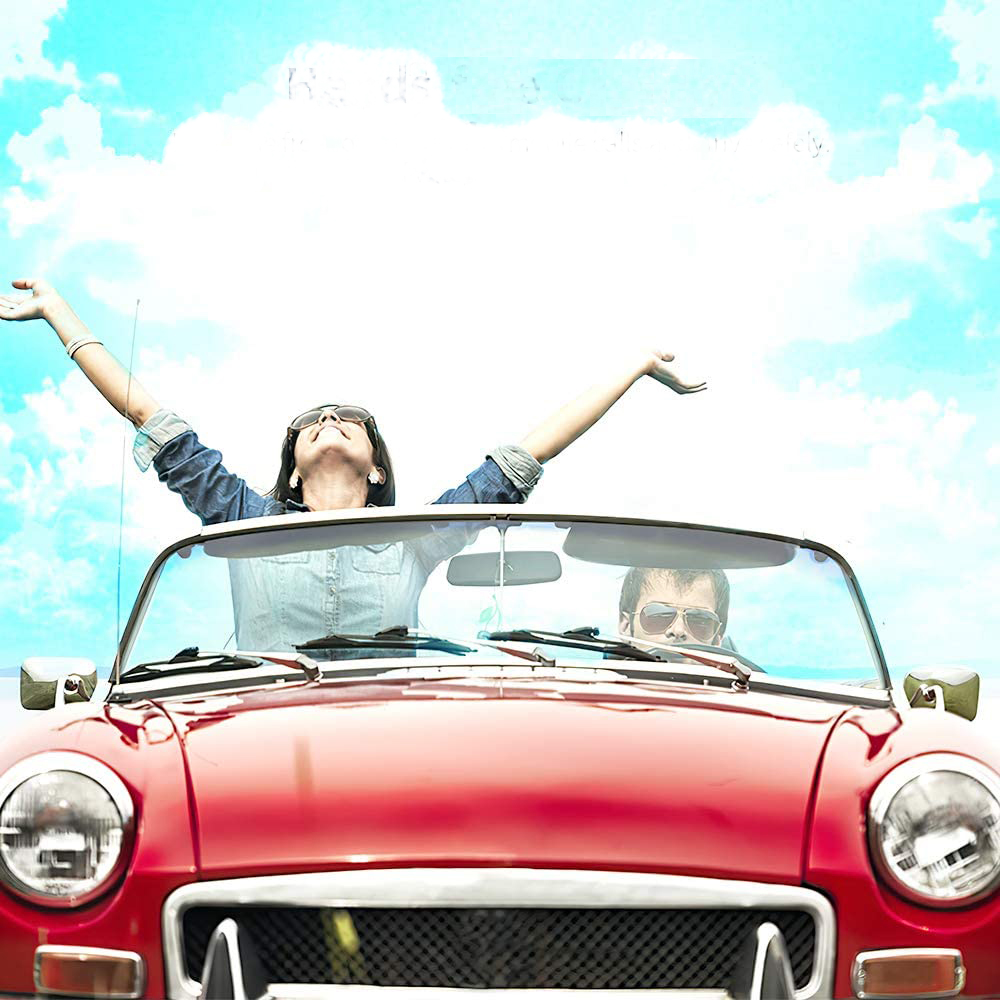 Ein Paar in einem roten Cabrio mit erhobenen Armen unter blauem Himmel mit Wolken.