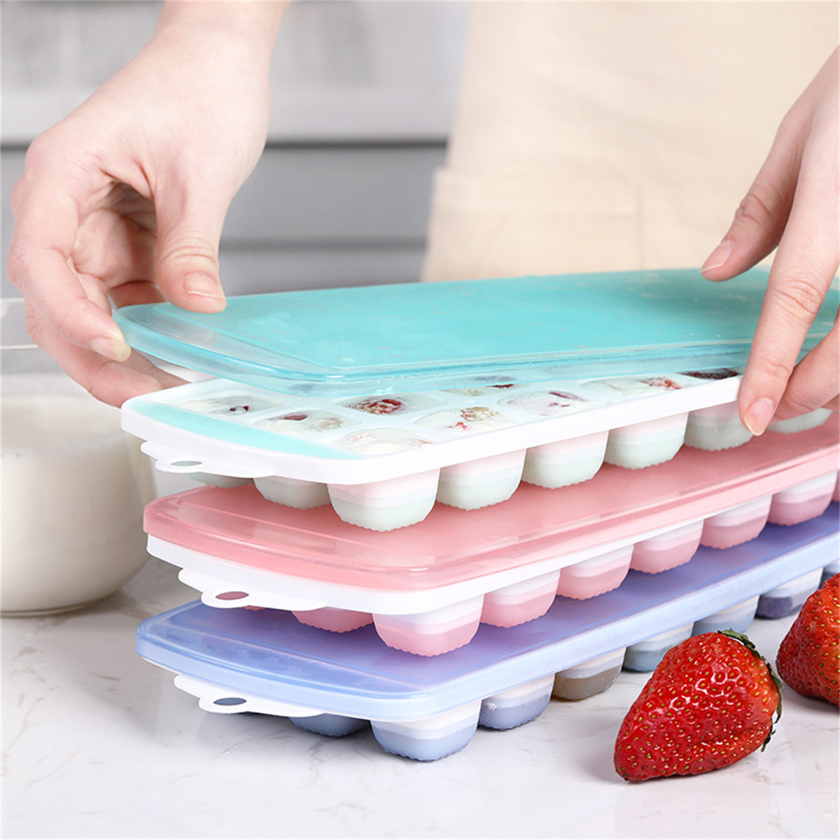 Eine Hand hält eine Eiswürfelschale mit verschiedenen gefrorenen Früchten. Eiswürfel mit Früchten und Getränken sind abgebildet.