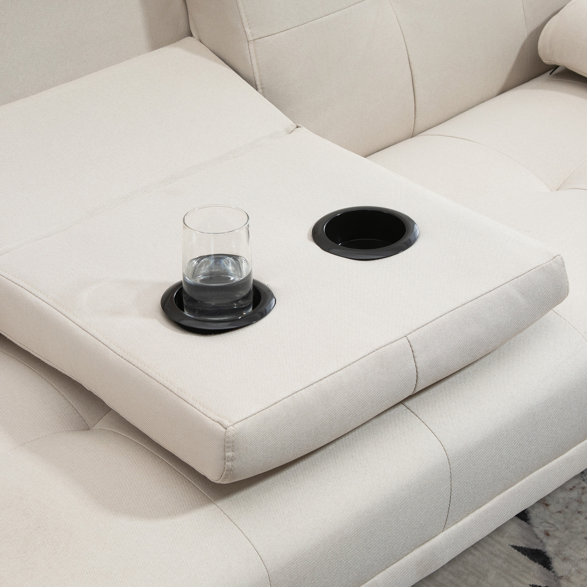 Cremefarbenes Sofa mit Getränkehalter. Ein Glas Wasser steht auf dem Getränkehalter. Knopfgitter.