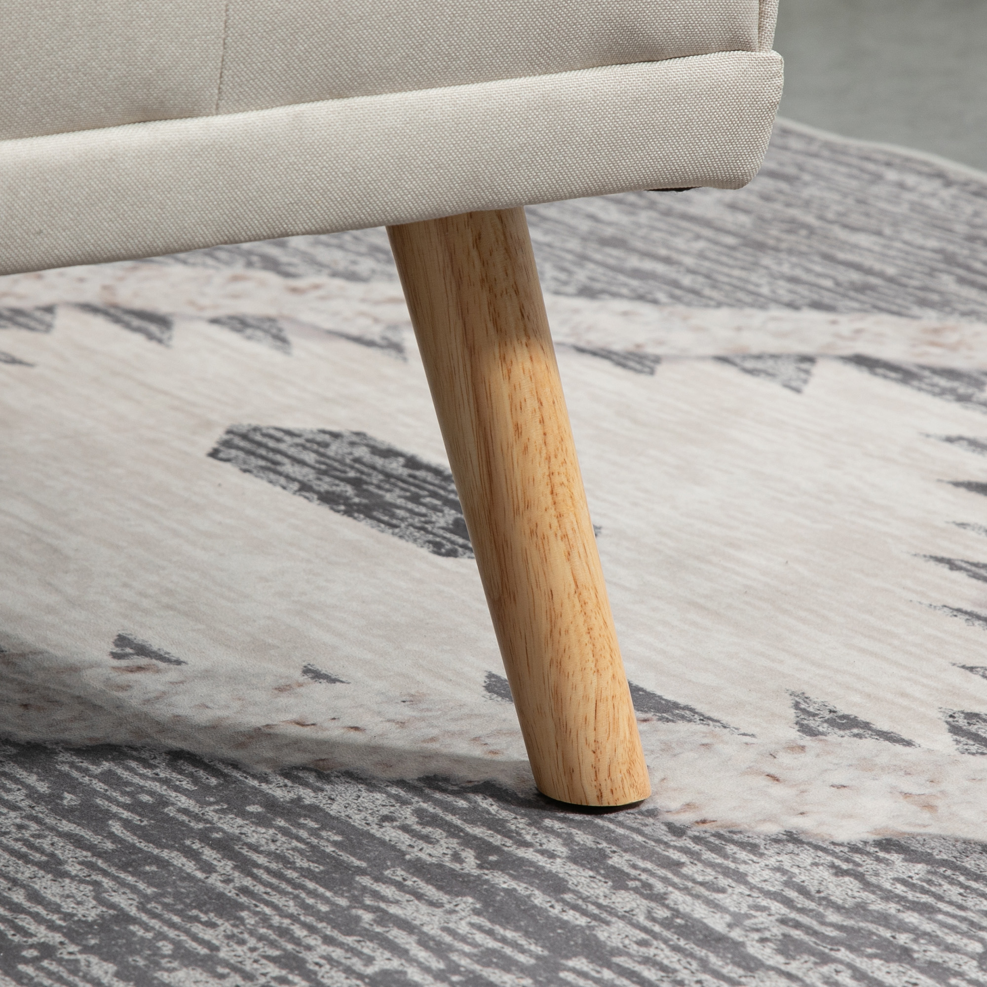 Bein eines beigen Sofas aus Holz, das auf einem gemusterten grauen Teppich ruht, Nahaufnahme.