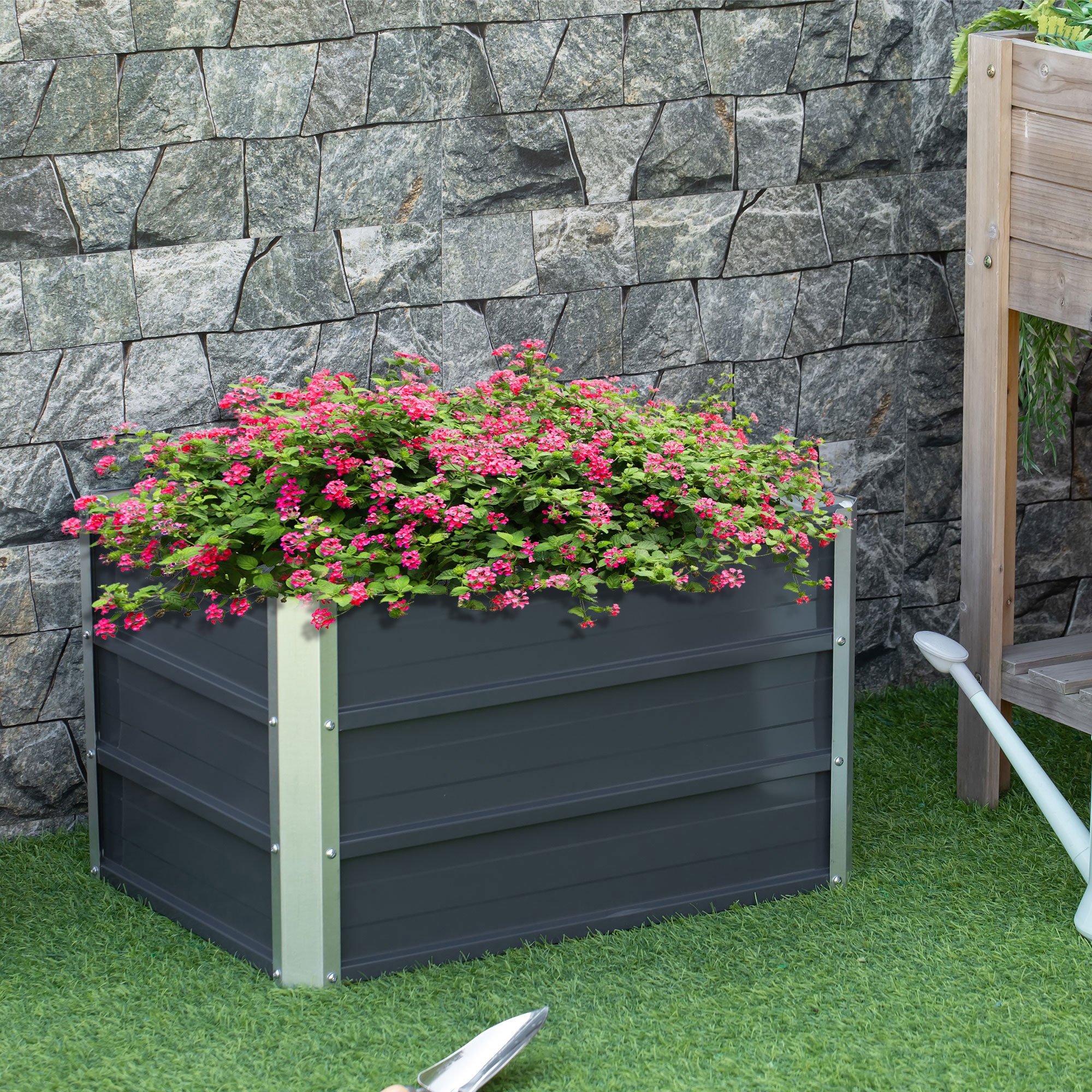Dunkelgrauer Pflanzkübel mit rosa Blumen, vor einem Steinwandhintergrund.