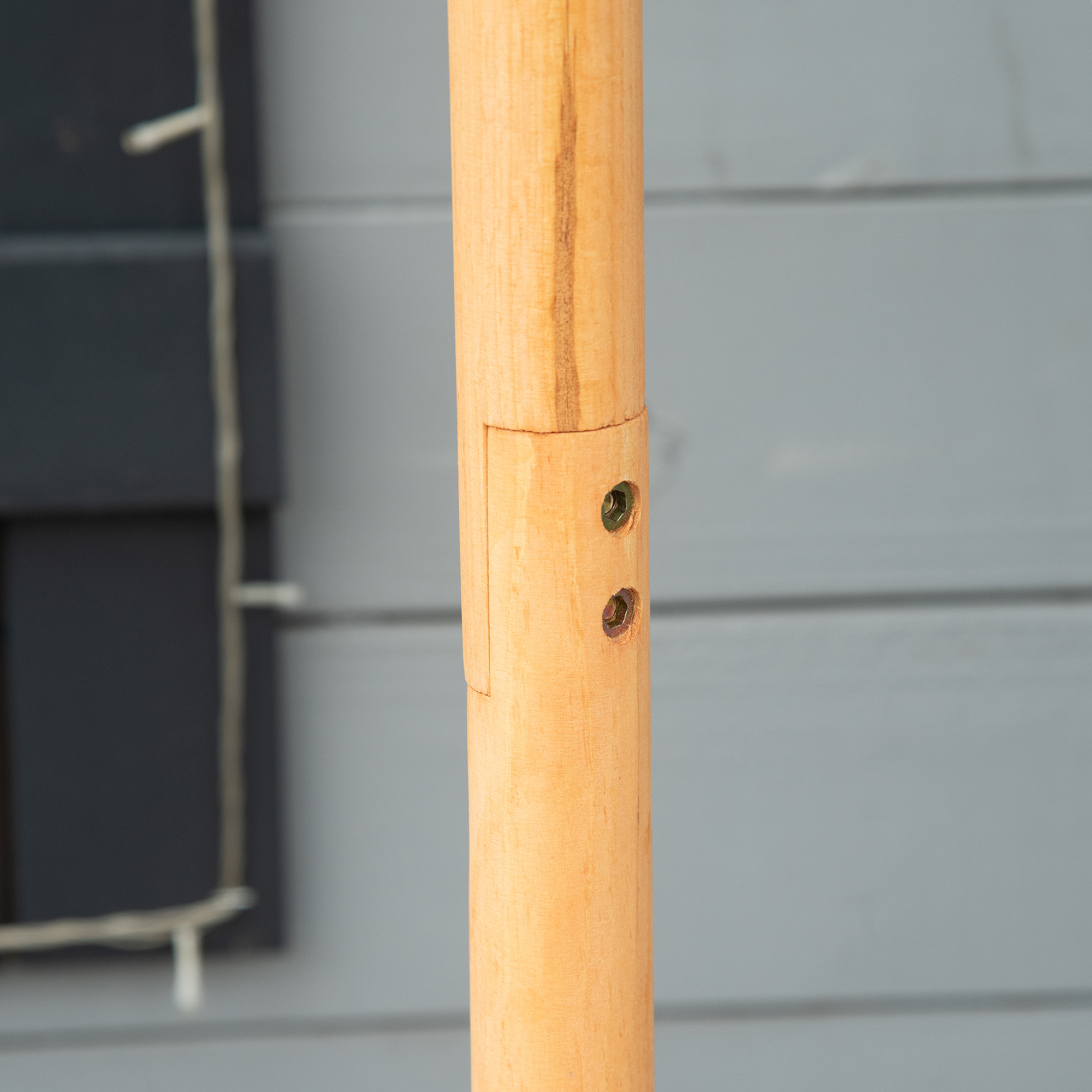 Eine Holzstange mit zwei Schrauben. Der Hintergrund ist eine verschwommene, hellblaue Wand.