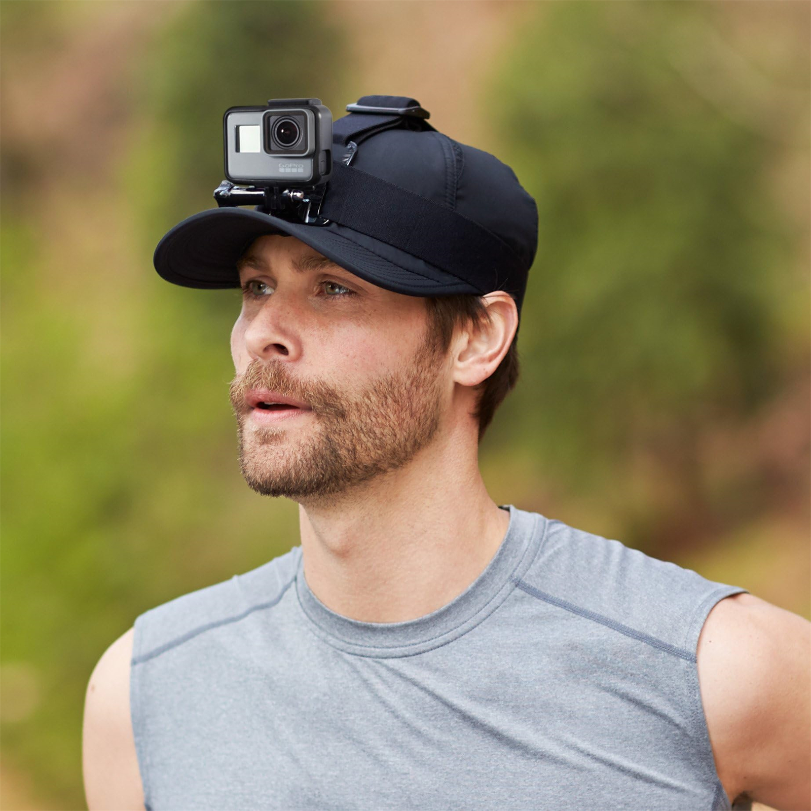Ein Mann, der eine Kappe mit einer GoPro-Kamera trägt, steht draußen mit grünem Hintergrund.