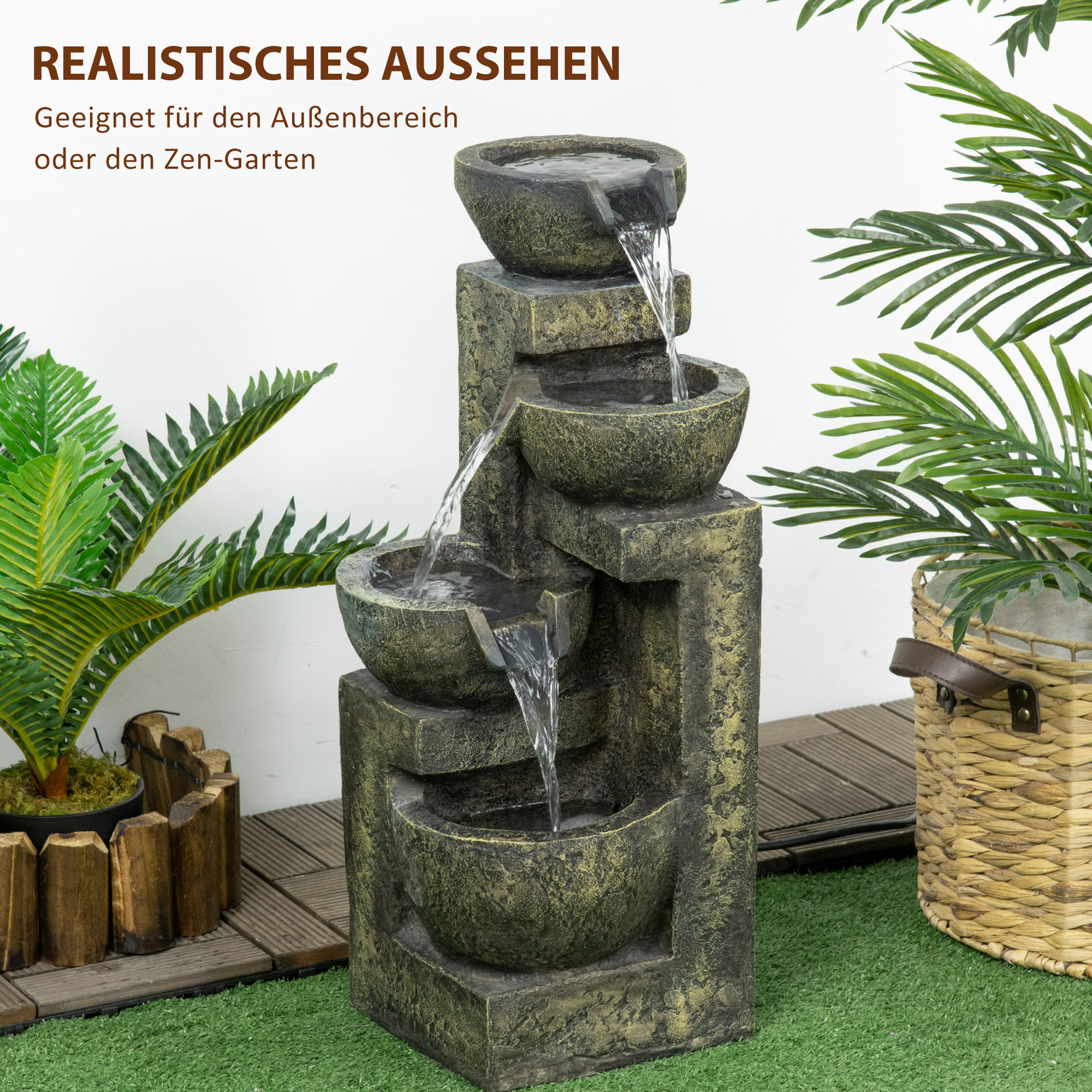 Steinartig gestufter Brunnen mit fließendem Wasser, umgeben von Pflanzen, auf grünem Gras.